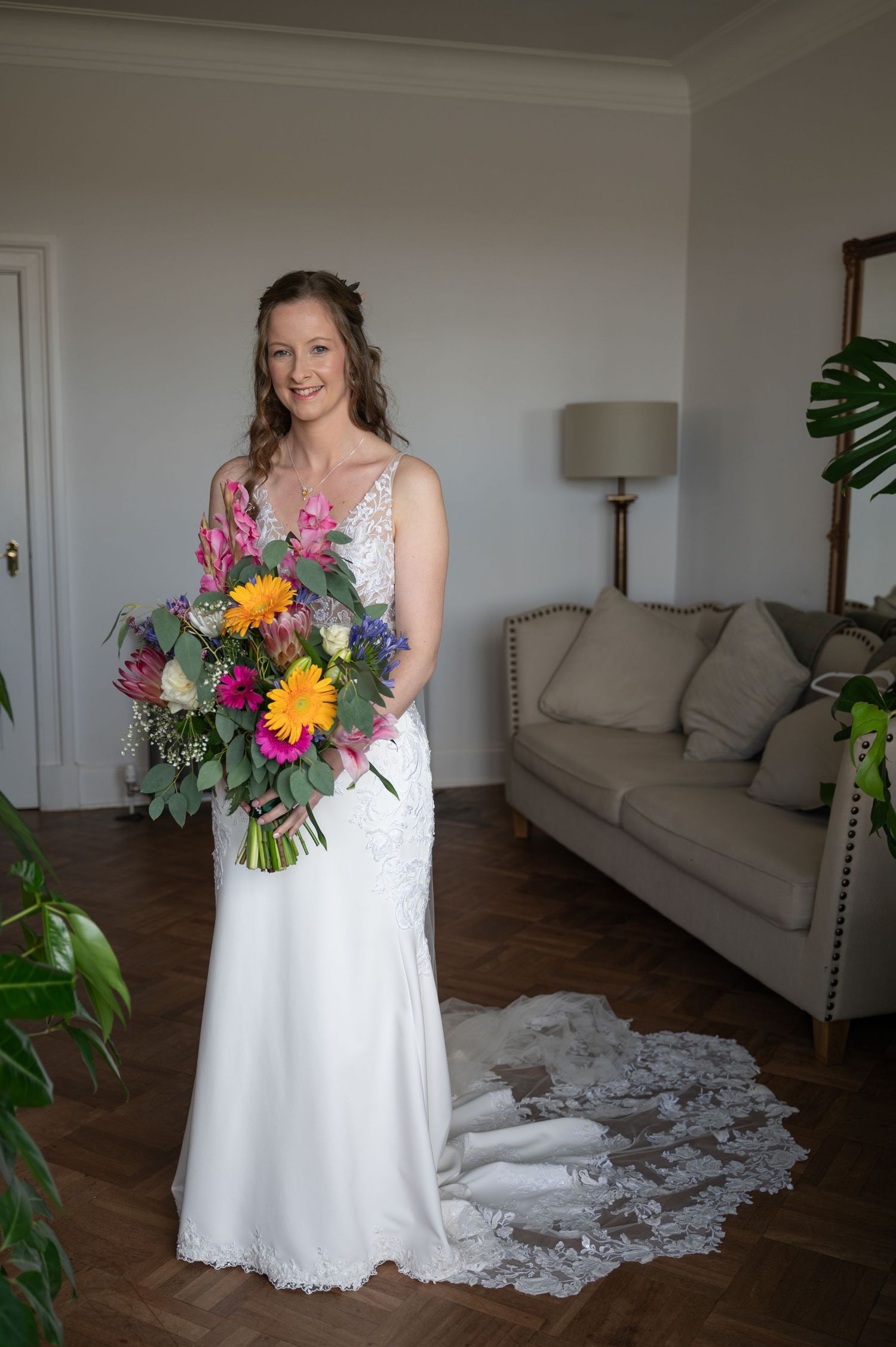 Bride standing in a softly lit living room, holding a bright, colourful bouquet