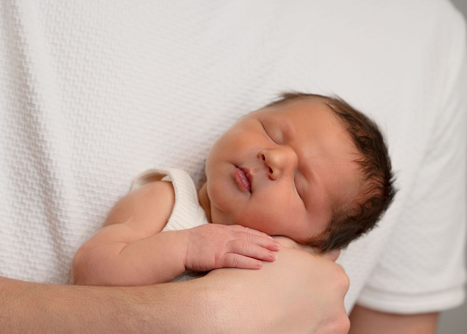 Sleeping newborn cradled in an adult’s arms.