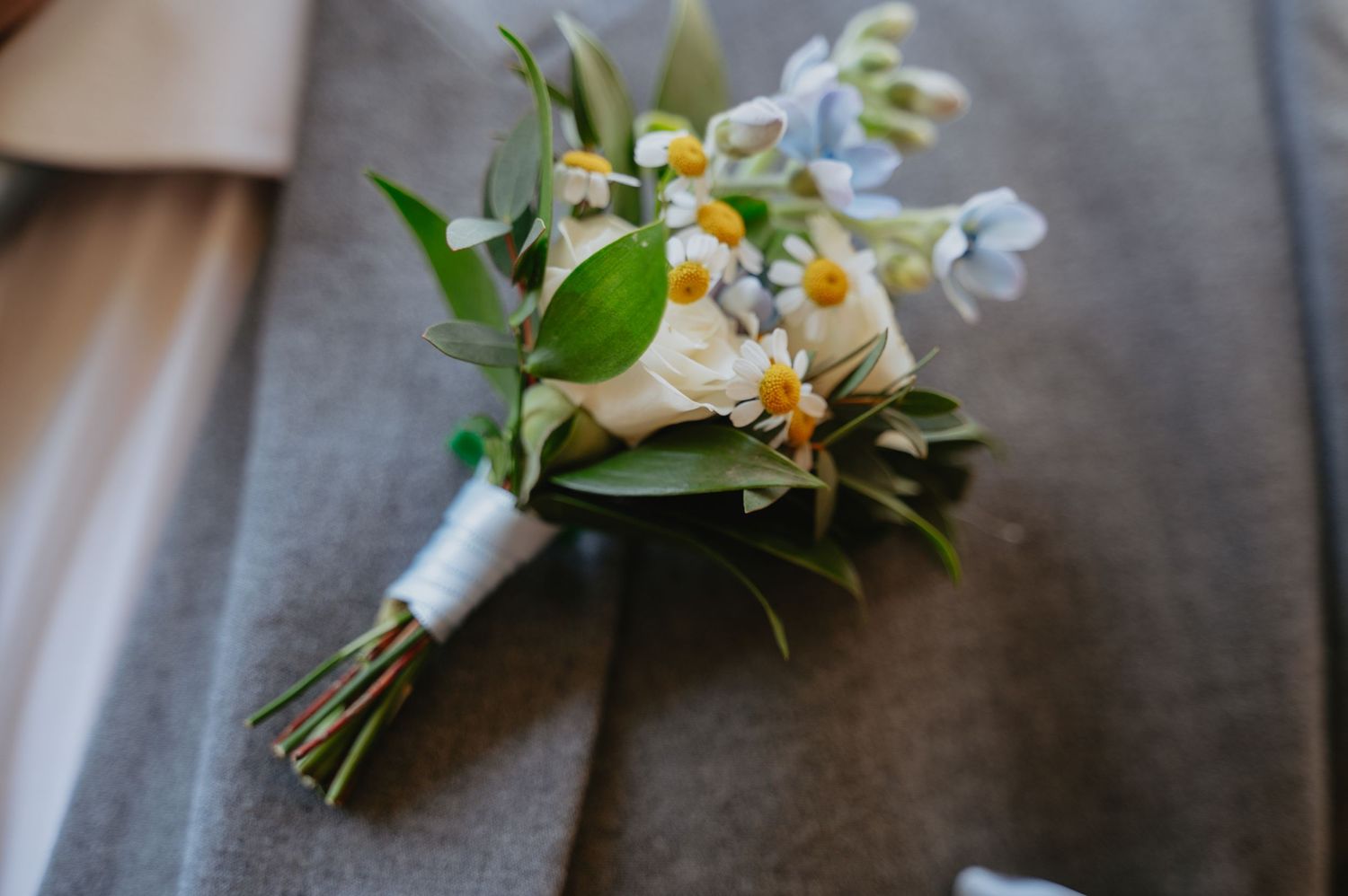 Close-up of a bridal bouquet with white, yellow, and green flowers resting on a rustic wooden floor before the ceremony.