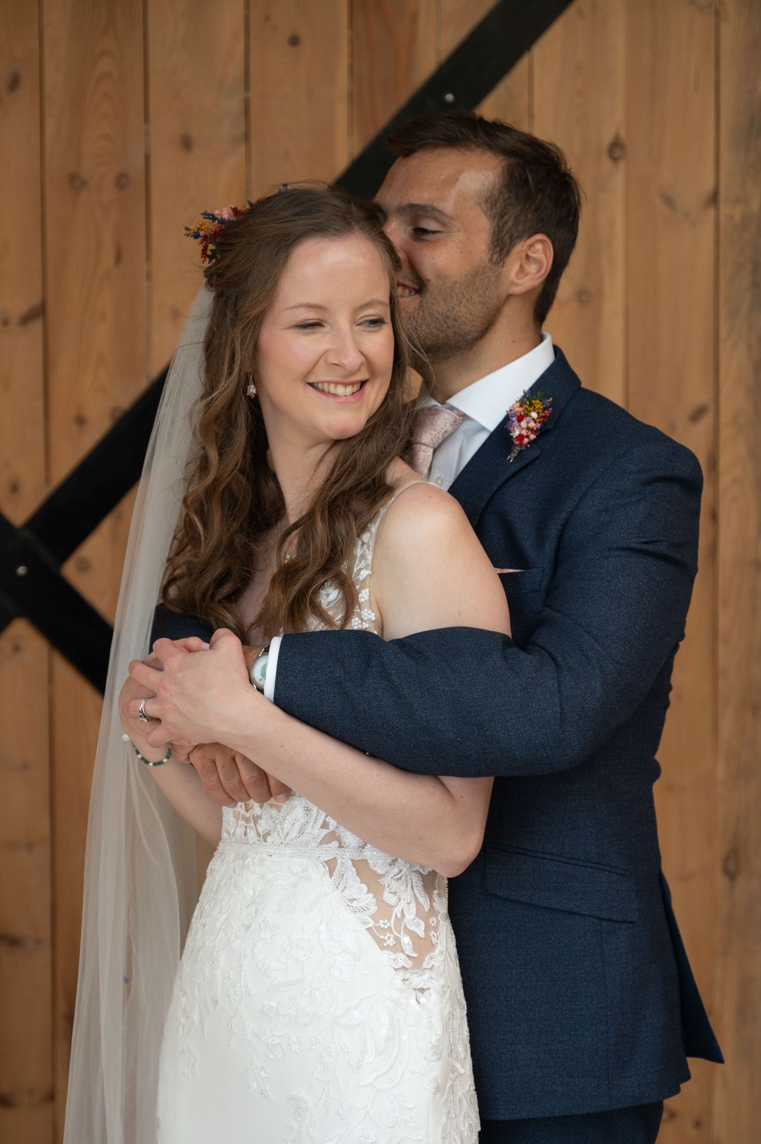 Bride and groom embracing in front of wooden backdrop, smiling