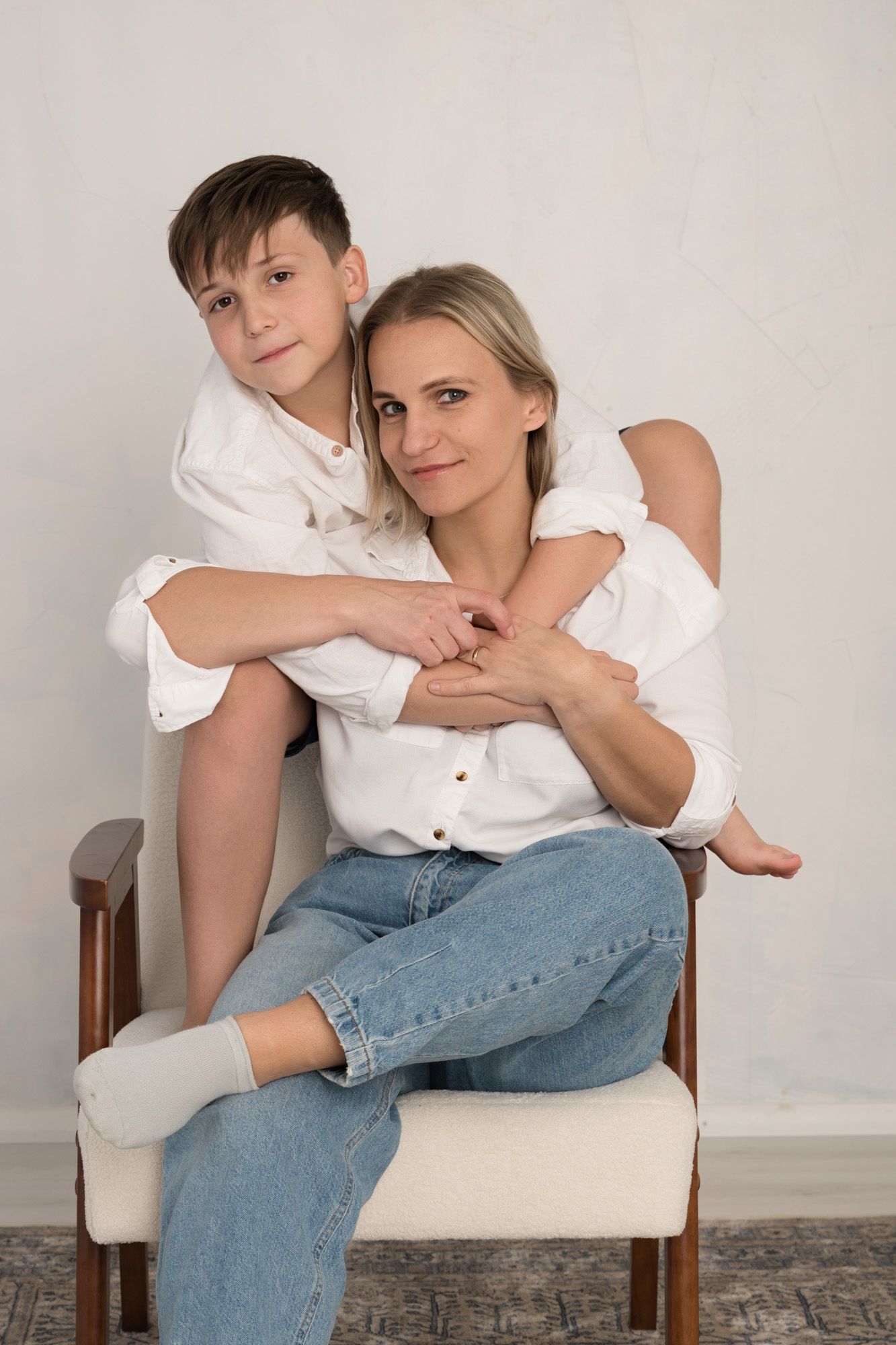 Woman sitting on a chair with a young boy leaning on her shoulders.