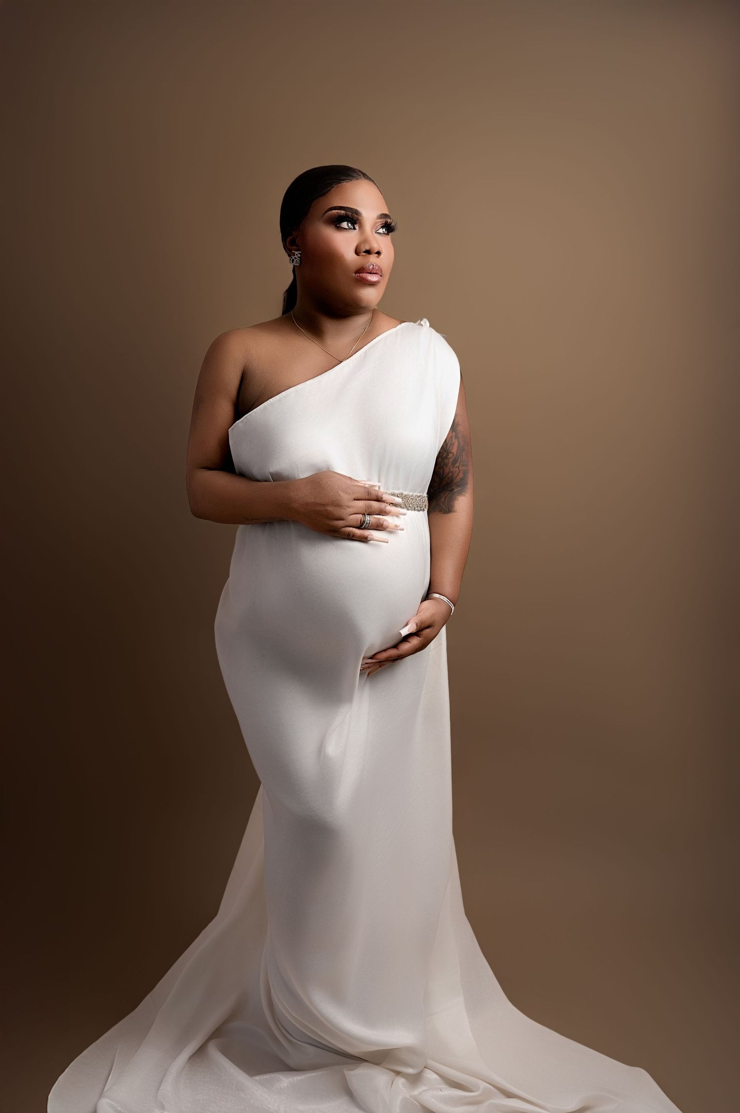 Pregnant woman wearing a white gown with a mermaid silhouette, cradling her belly with both hands and softly smiling,