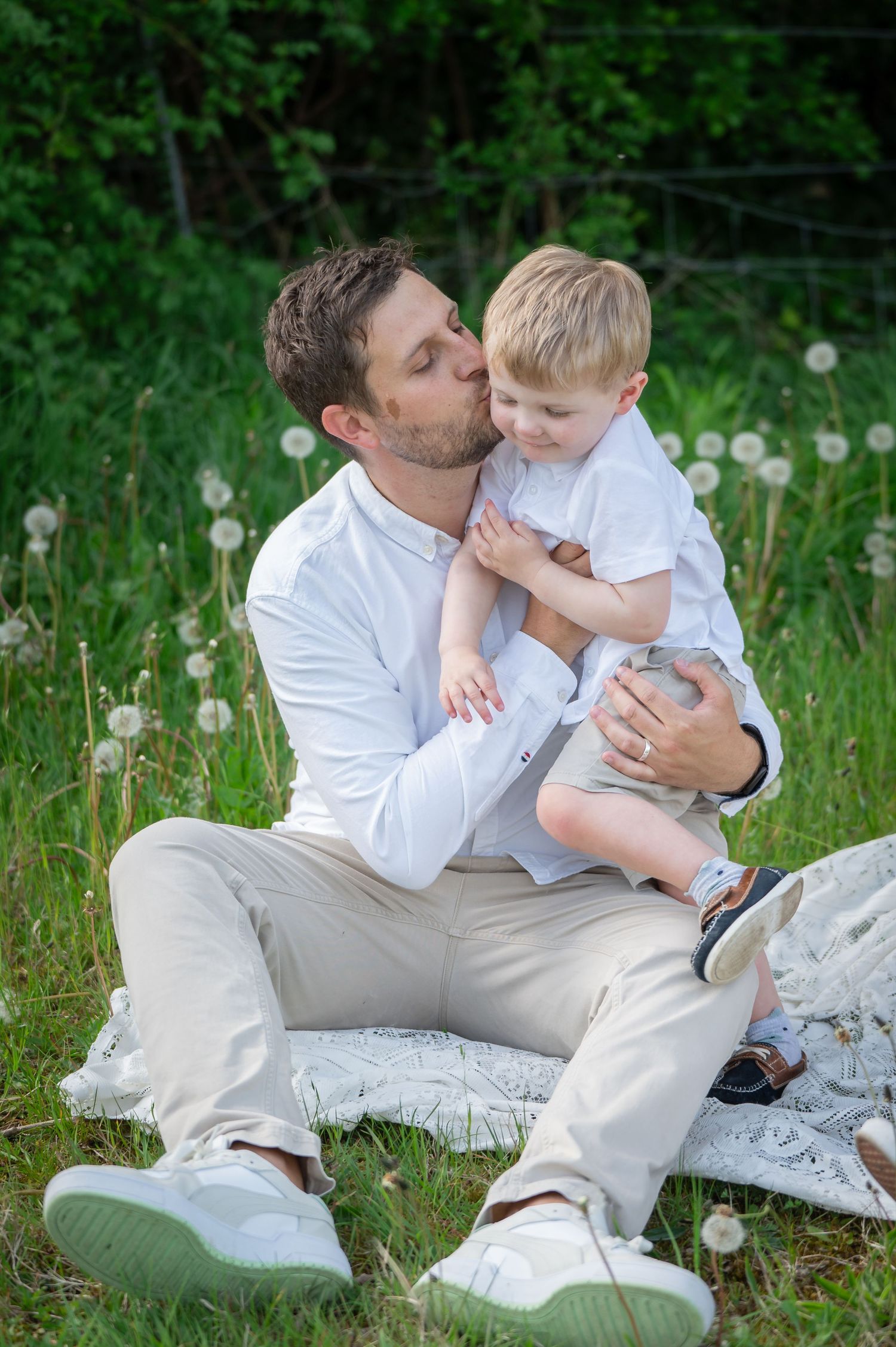Father holding his child close while sitting in the grass, both smiling and sharing a quiet, loving moment in nature.