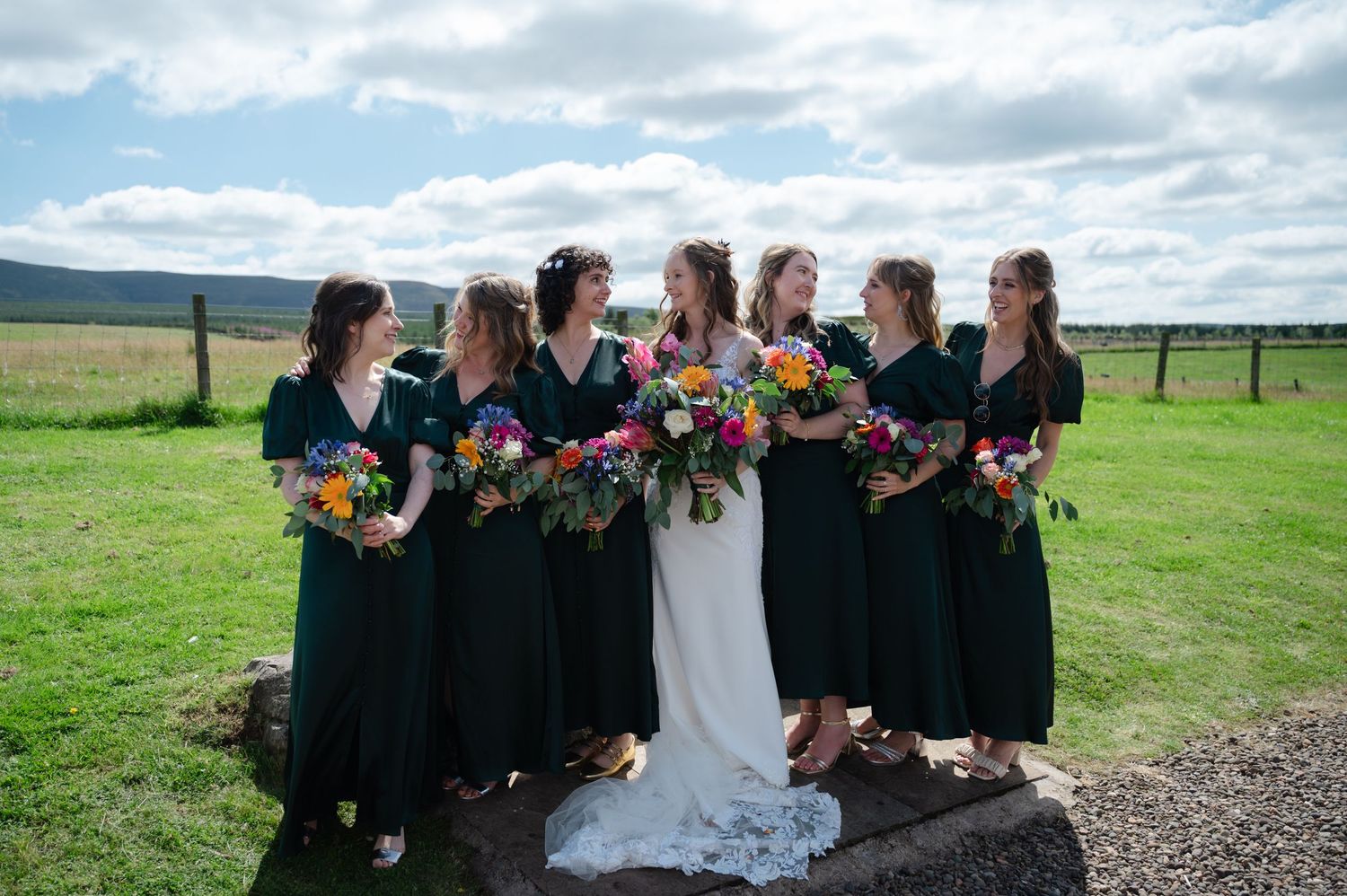 Bride and bridesmaids laughing and chatting during group photo outdoors