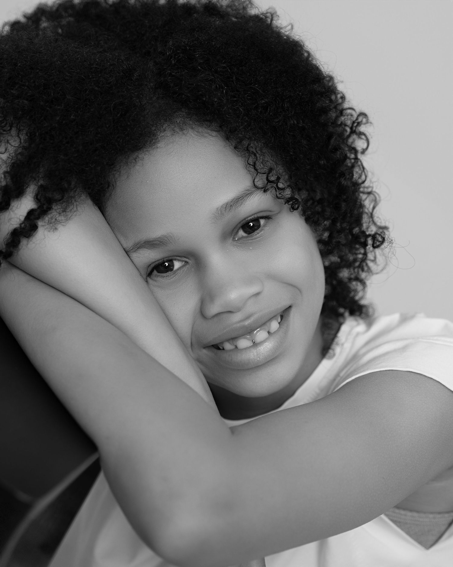 Black and white portrait of a smiling girl with curly hair, lying down with a relaxed pose and joyful expression.