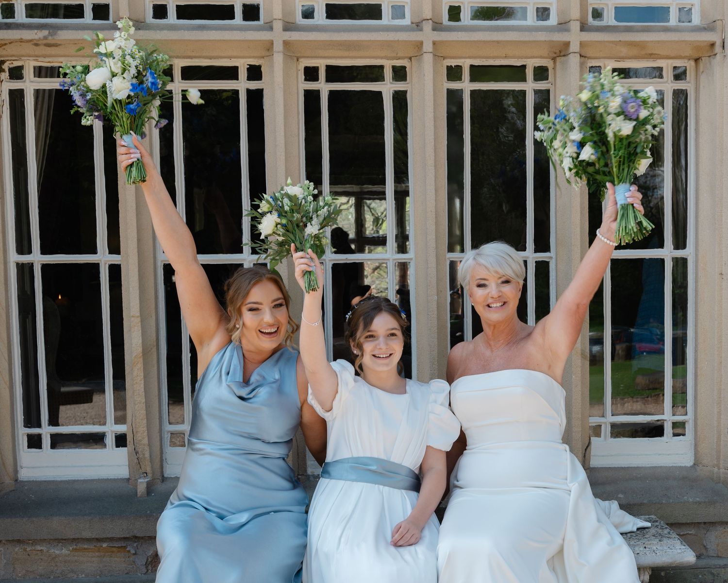 Bride and two bridesmaids cheerfully posing with raised bouquets.