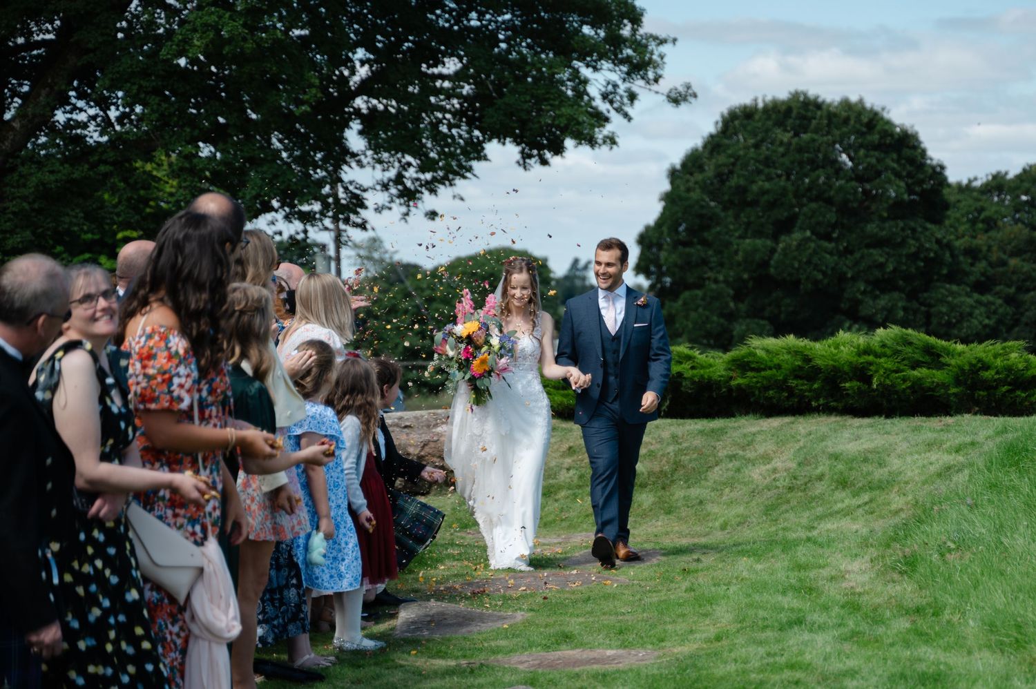 Bride and groom walking hand in hand outside as guests cheer from both sides