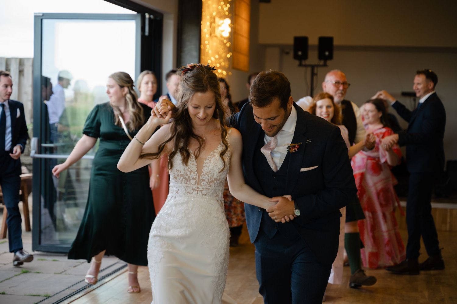 Newlyweds laughing and entering the reception room surrounded by guests