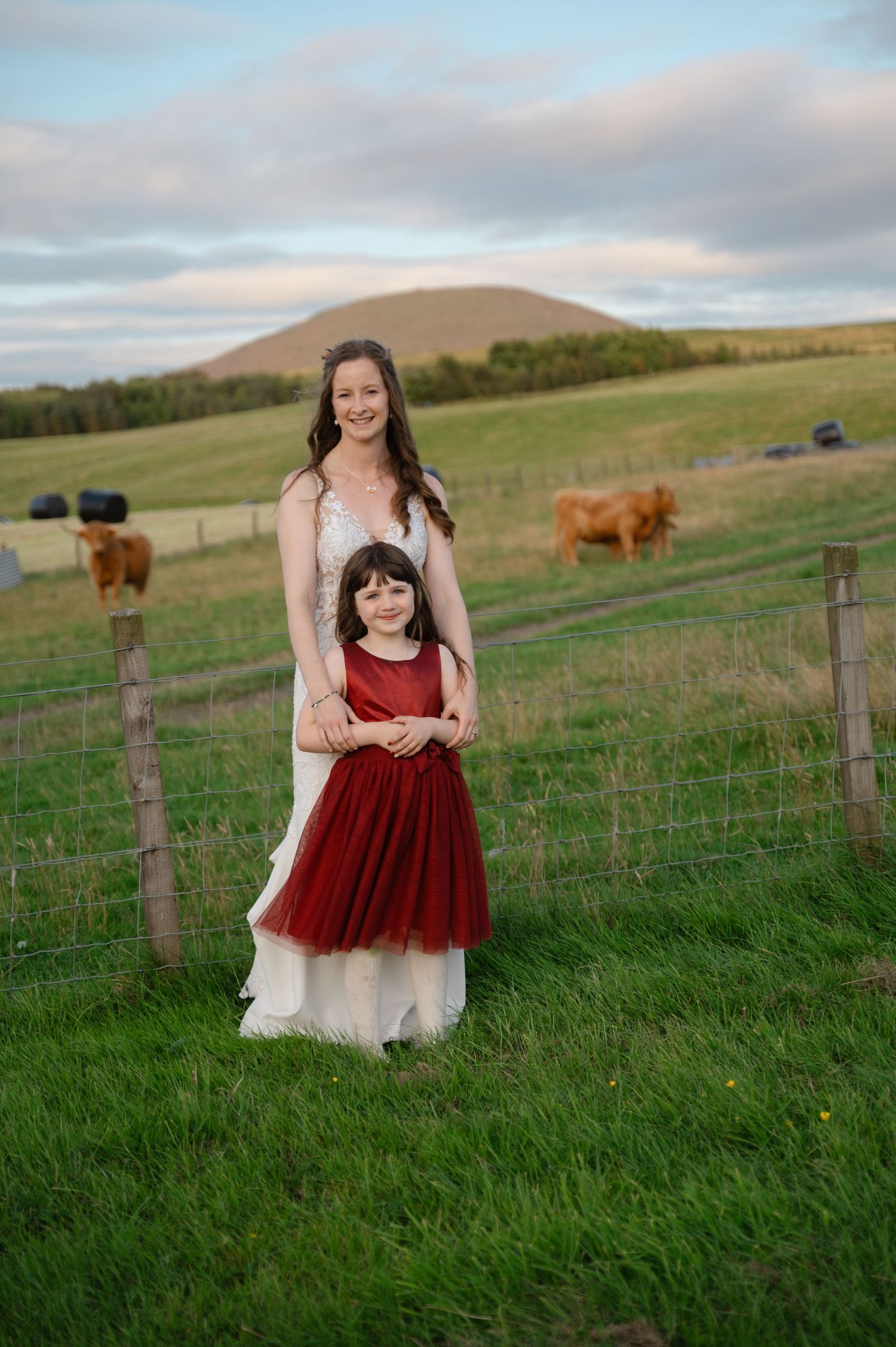 Young girl in red dress standing in open countryside field at wedding