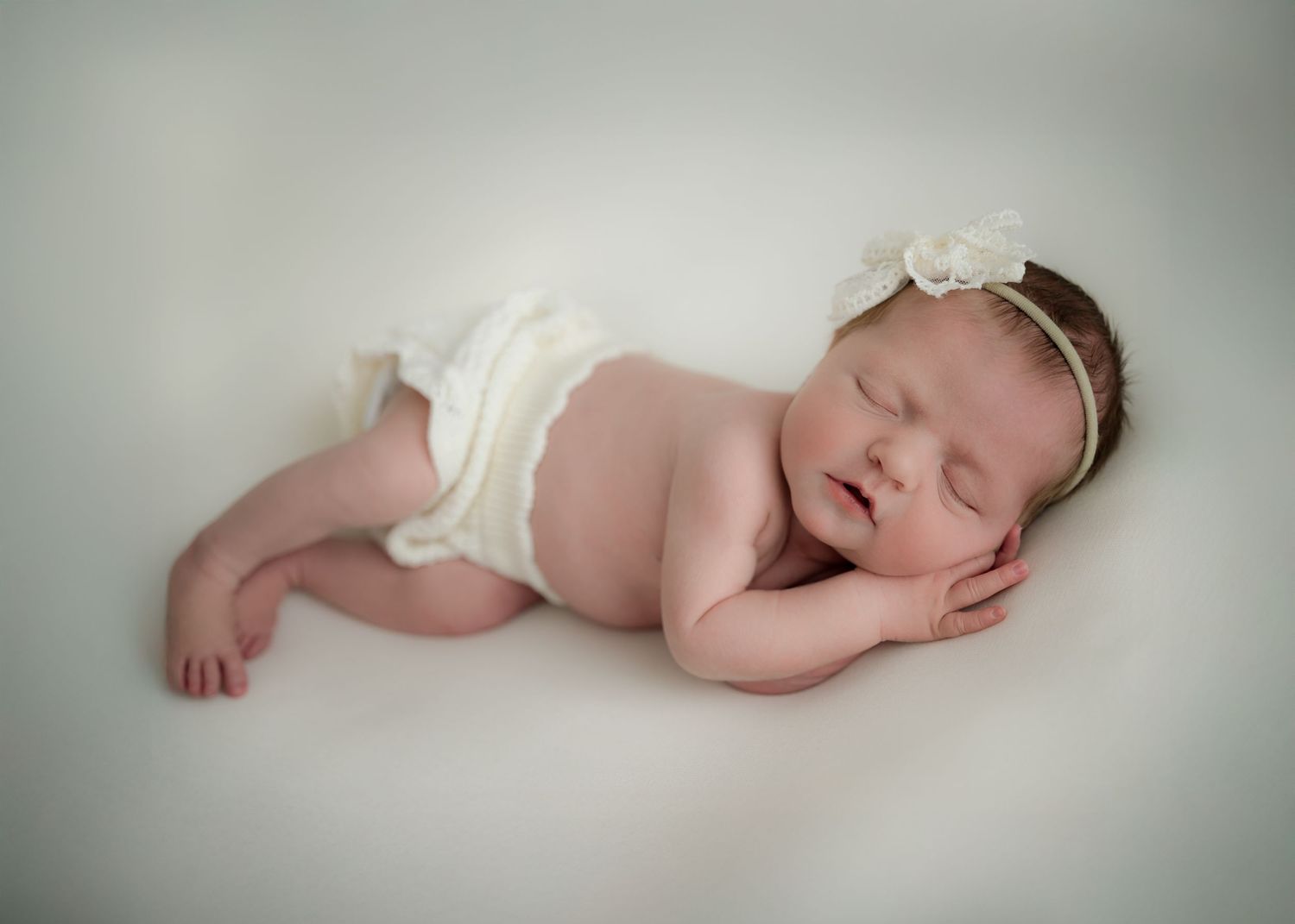 Newborn baby sleeping peacefully on a white blanket, wearing a delicate headband.