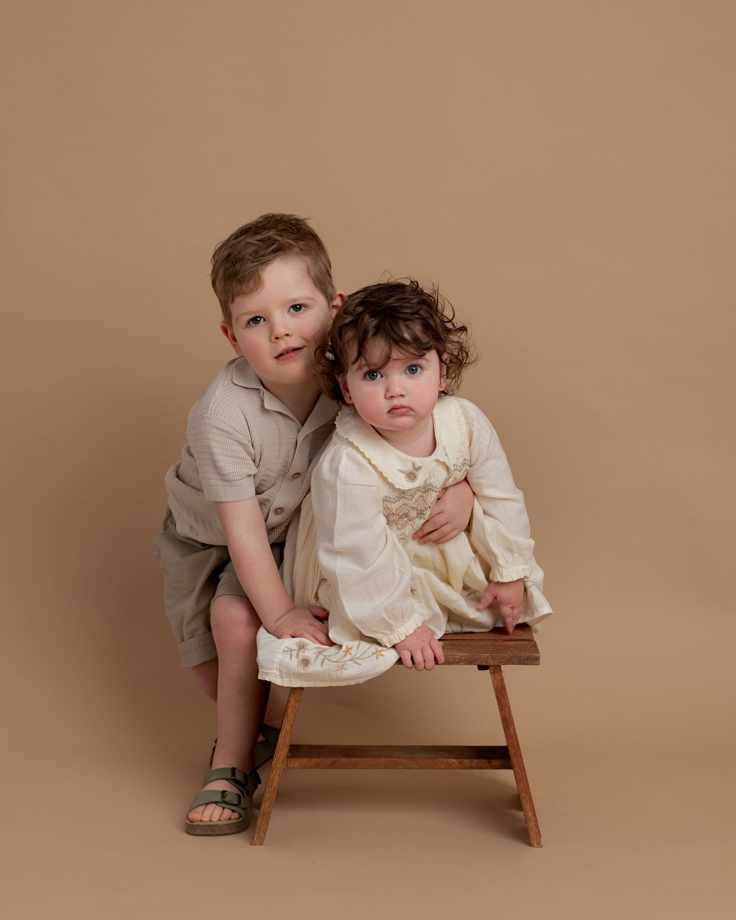 Toddler girl wearing a cream dress holding flower petals during a studio child portrait session in Lancashire