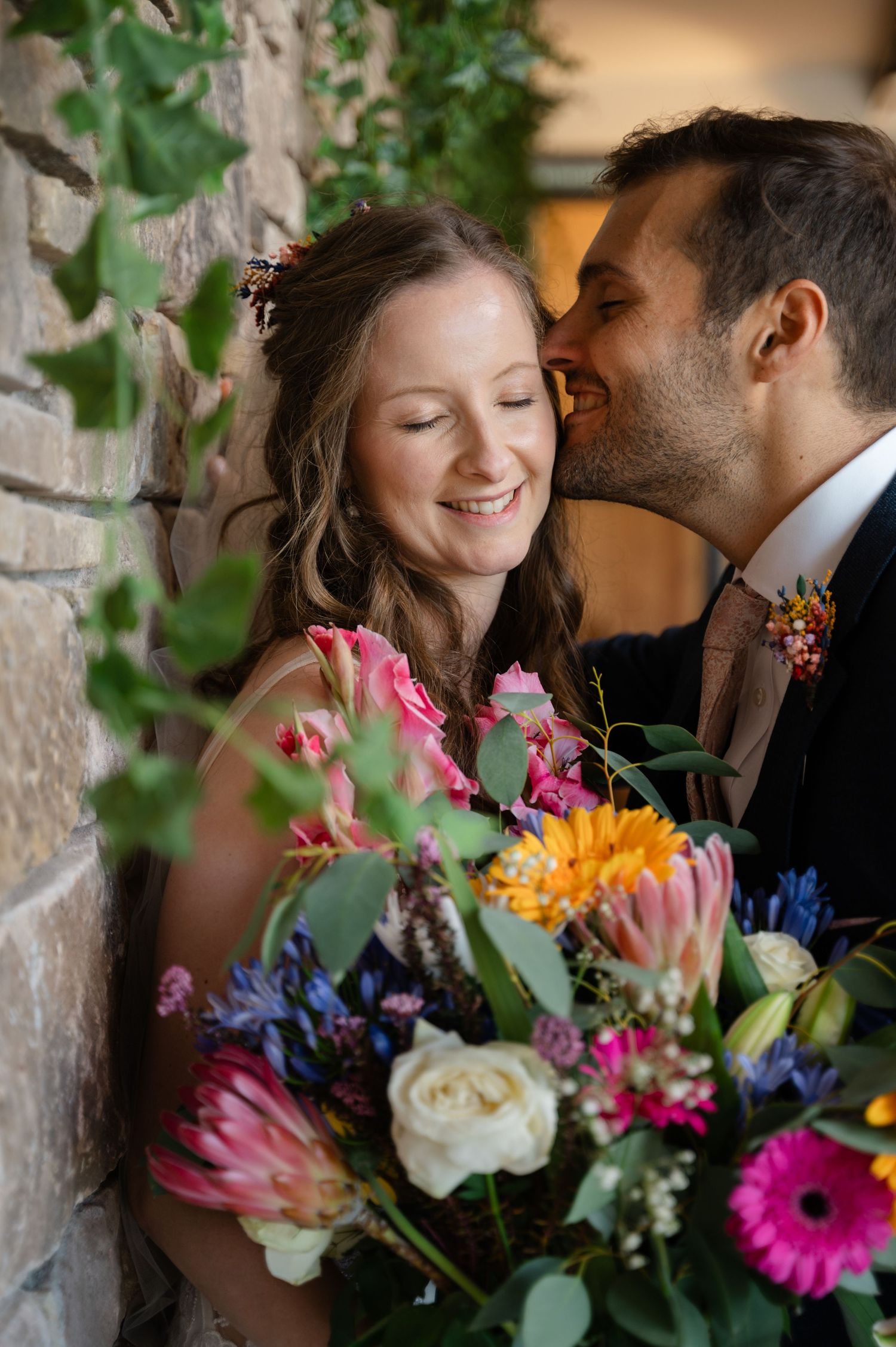 Bride and groom smiling closely with colourful bouquet of fresh flowers
