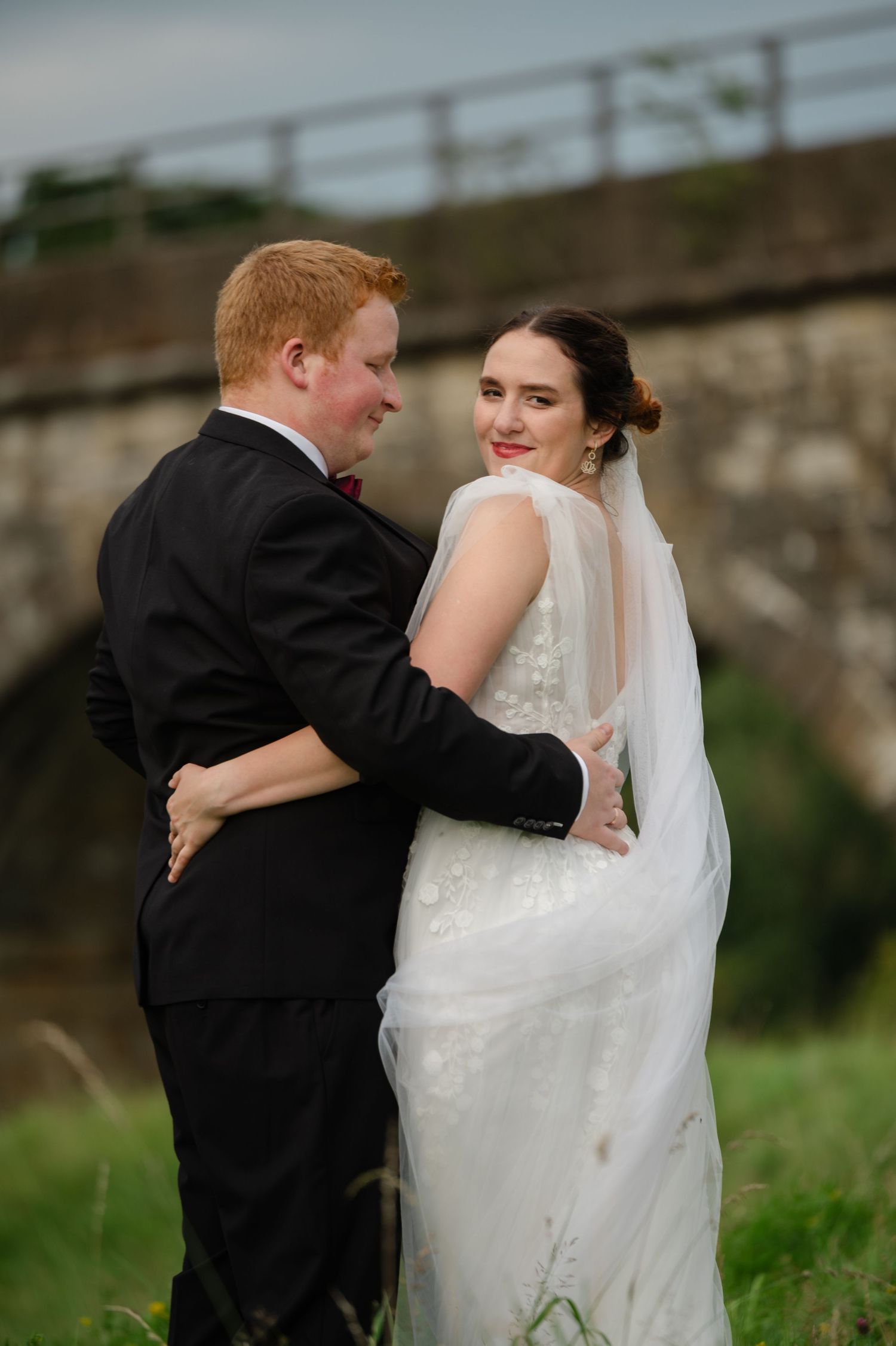 Bride and groom standing together near a viaduct, smiling at each other