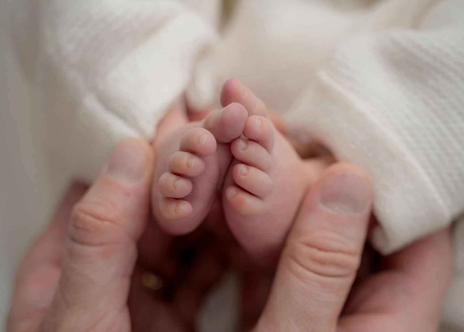 Close-up of newborn baby’s toes held by a parent’s hands.