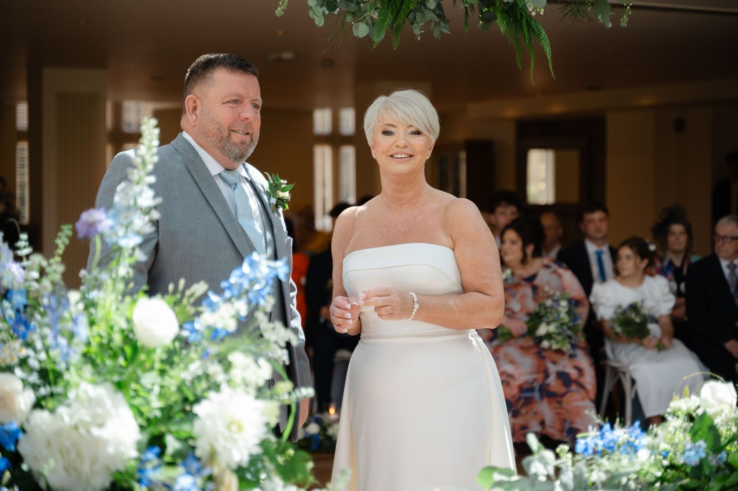 Bride and groom standing together at the altar during the wedding ceremony, with floral arrangements and guests in the background.