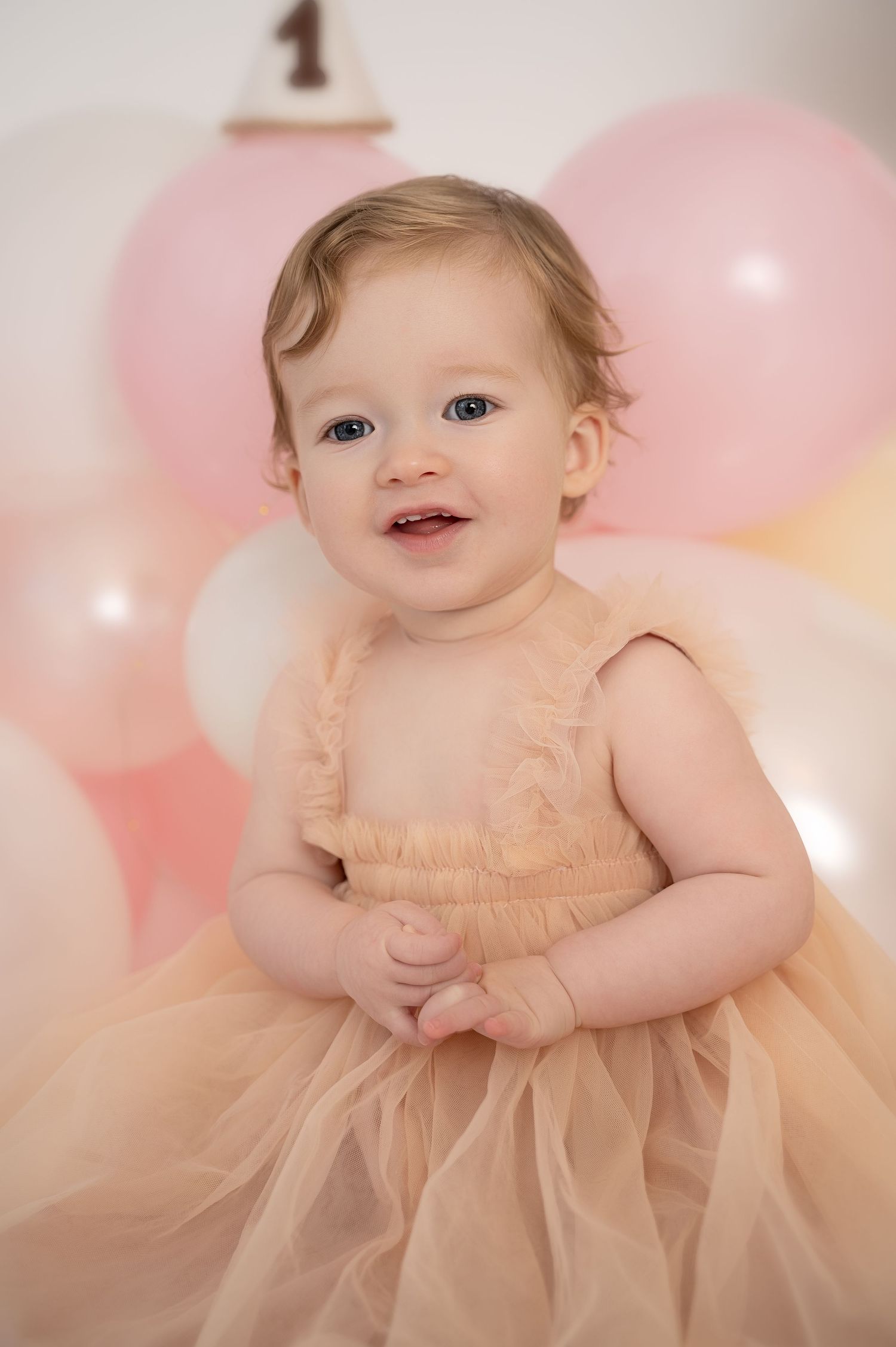 Baby sitting upright on a pink blanket, looking toward the camera.