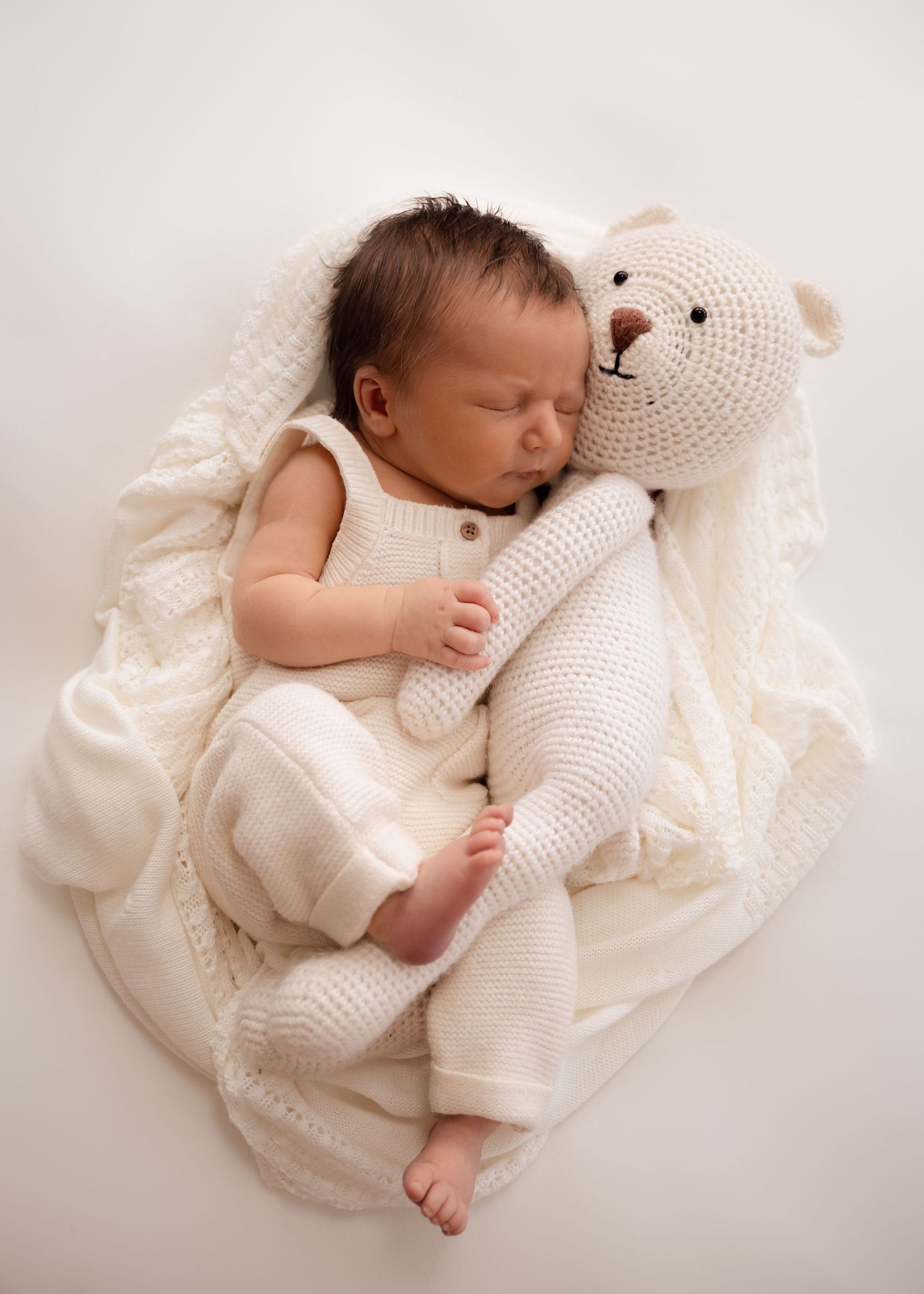 Newborn sleeping while cuddling a stuffed bear
