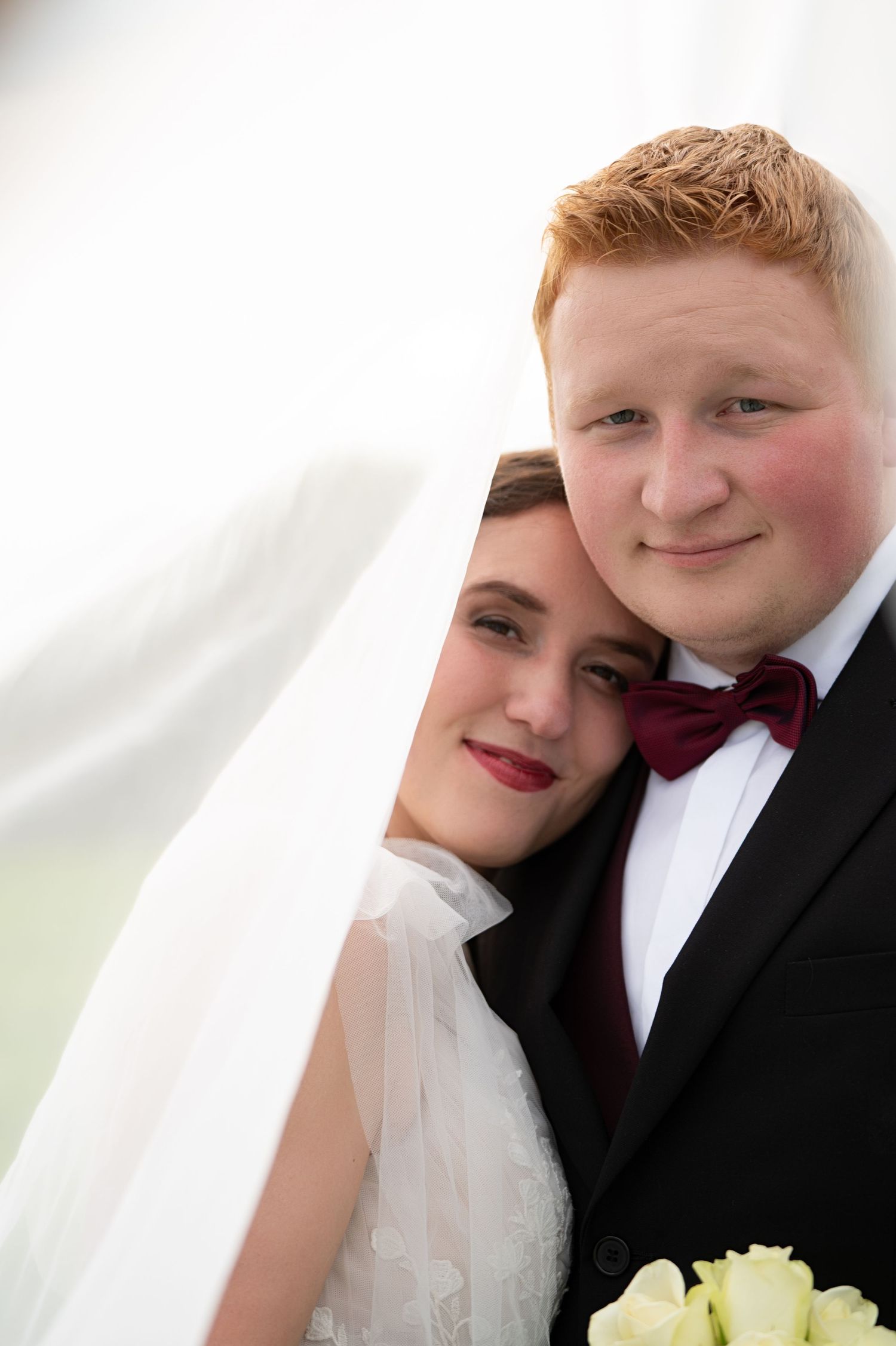 Bride and groom cuddled together, smiling under bride’s veil