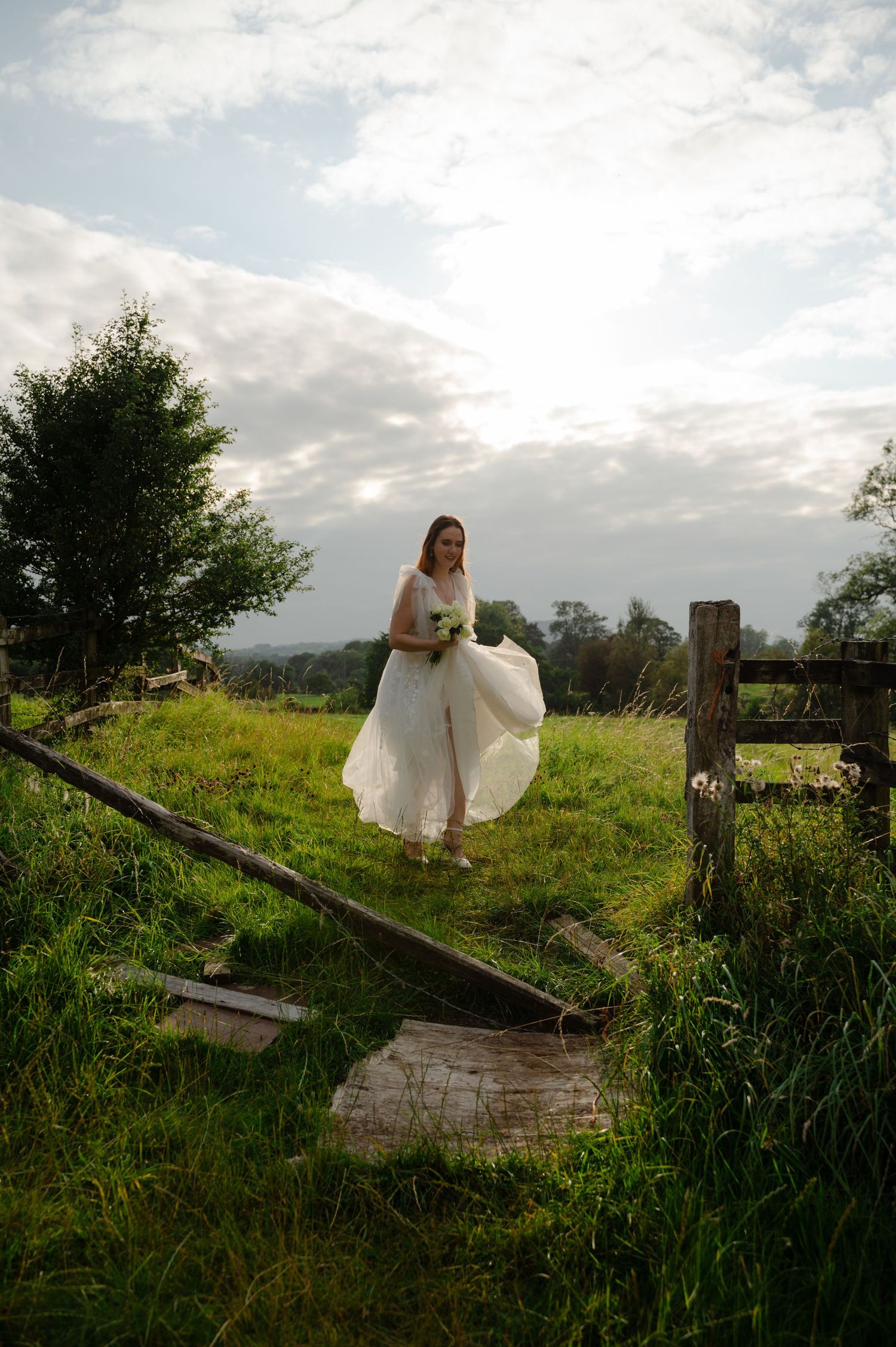 Bride walking alone through a field with a moody sky overhead