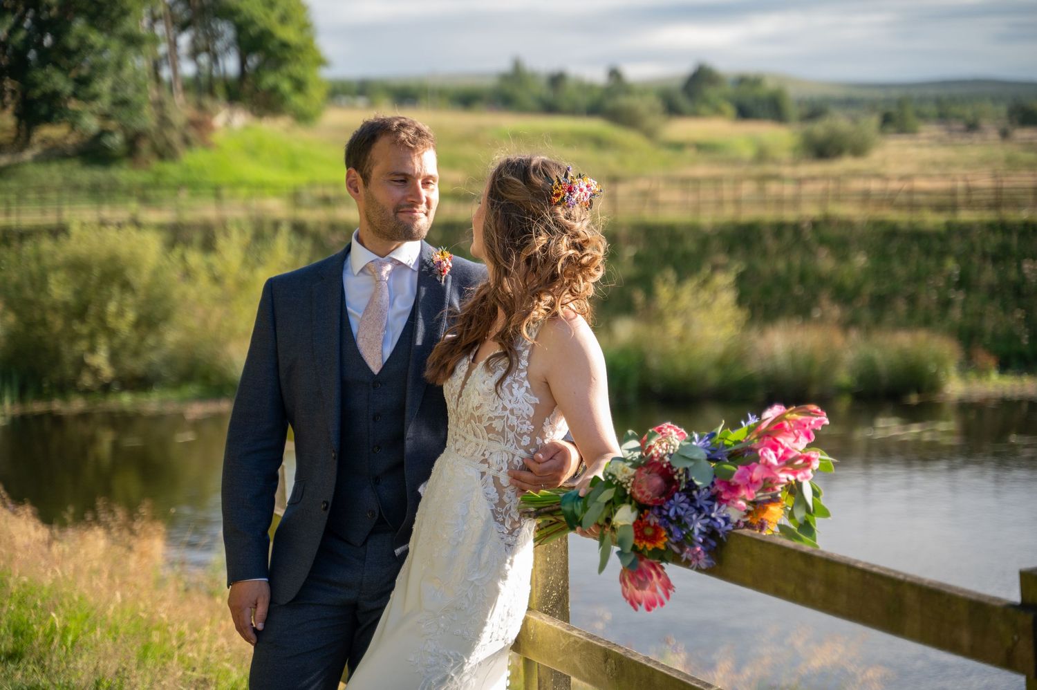 Wedding couple smiling together near a wooden fence and lake