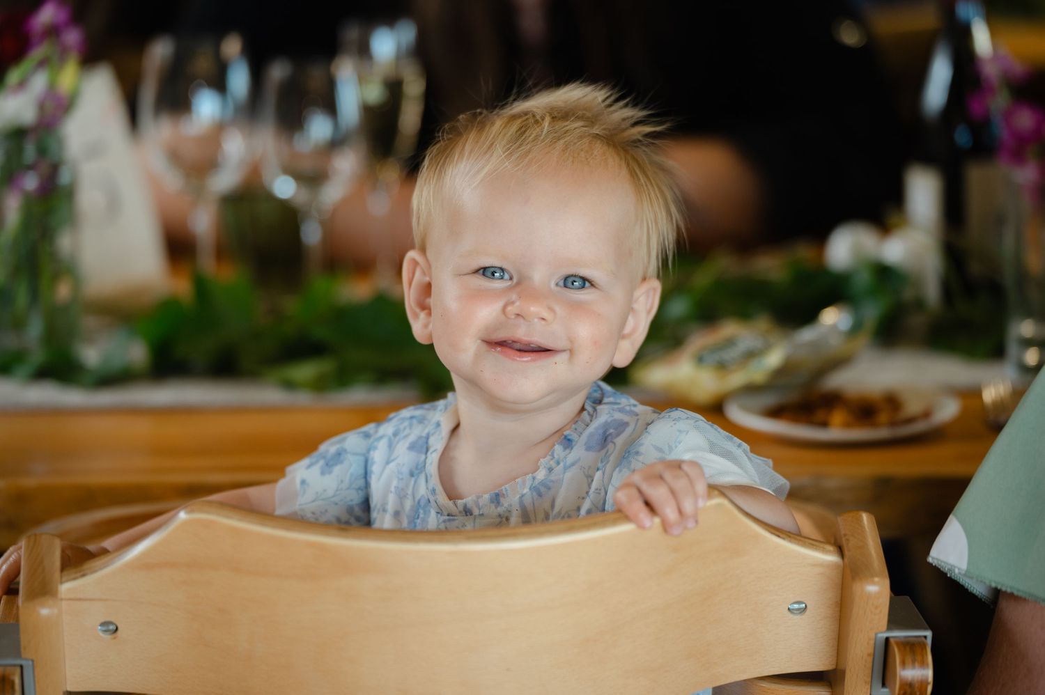 Young girl smiling while sitting at a wooden table during a wedding celebration