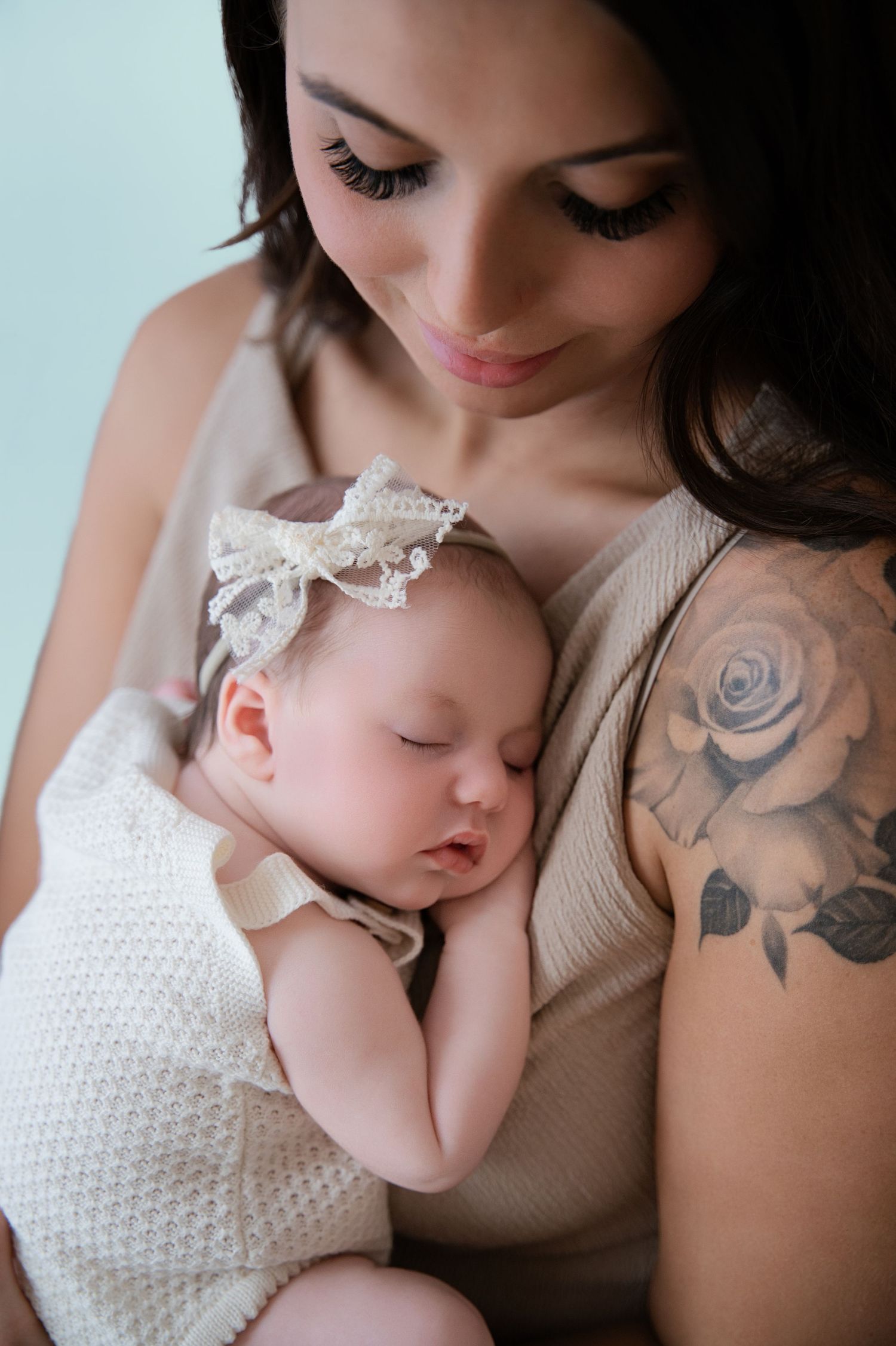 Mother holding a sleeping newborn close to her chest, with a gentle expression and floral tattoo visible on her arm.