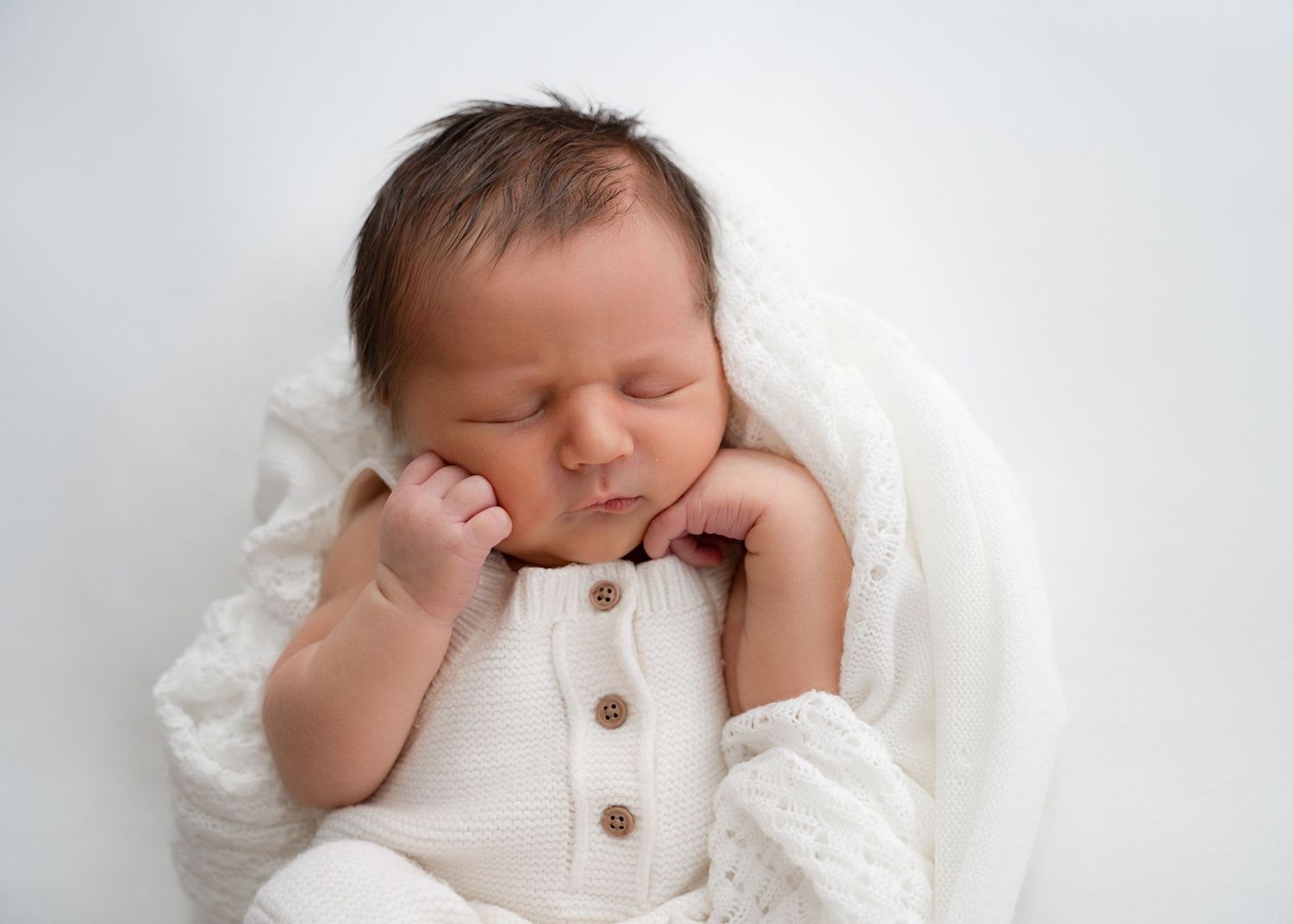 Newborn baby in a white romper stretching on a white blanket