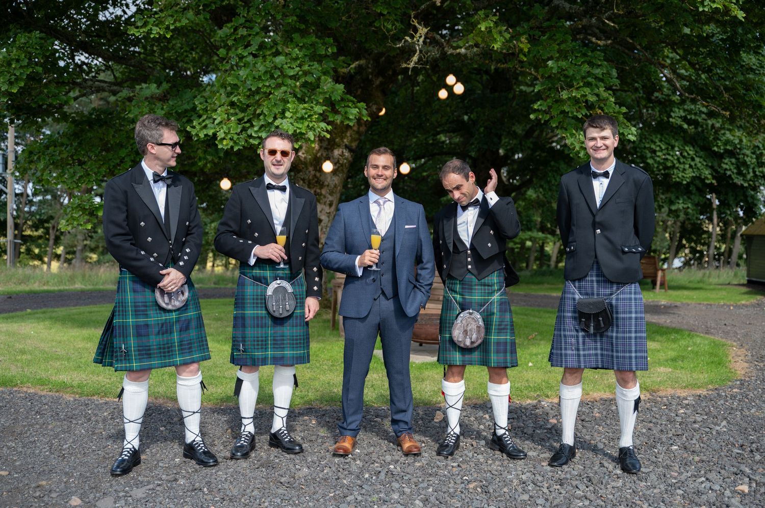 Groomsmen standing outdoors in kilts, smiling and dressed for the wedding ceremony