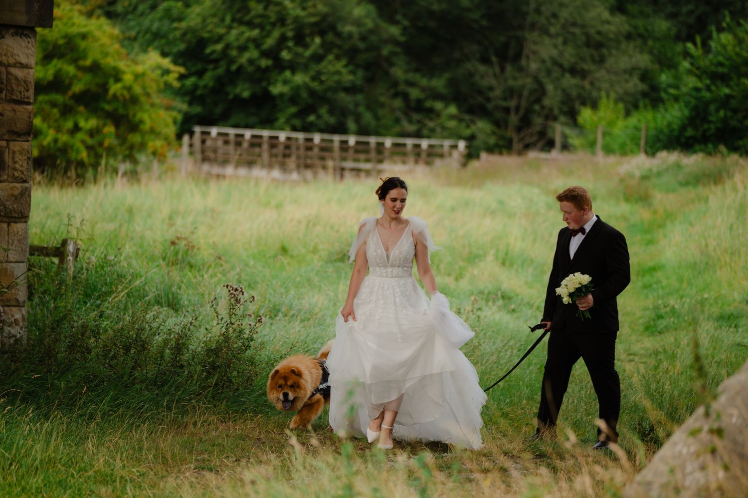 Bride and groom walking through a field with their dog beside them