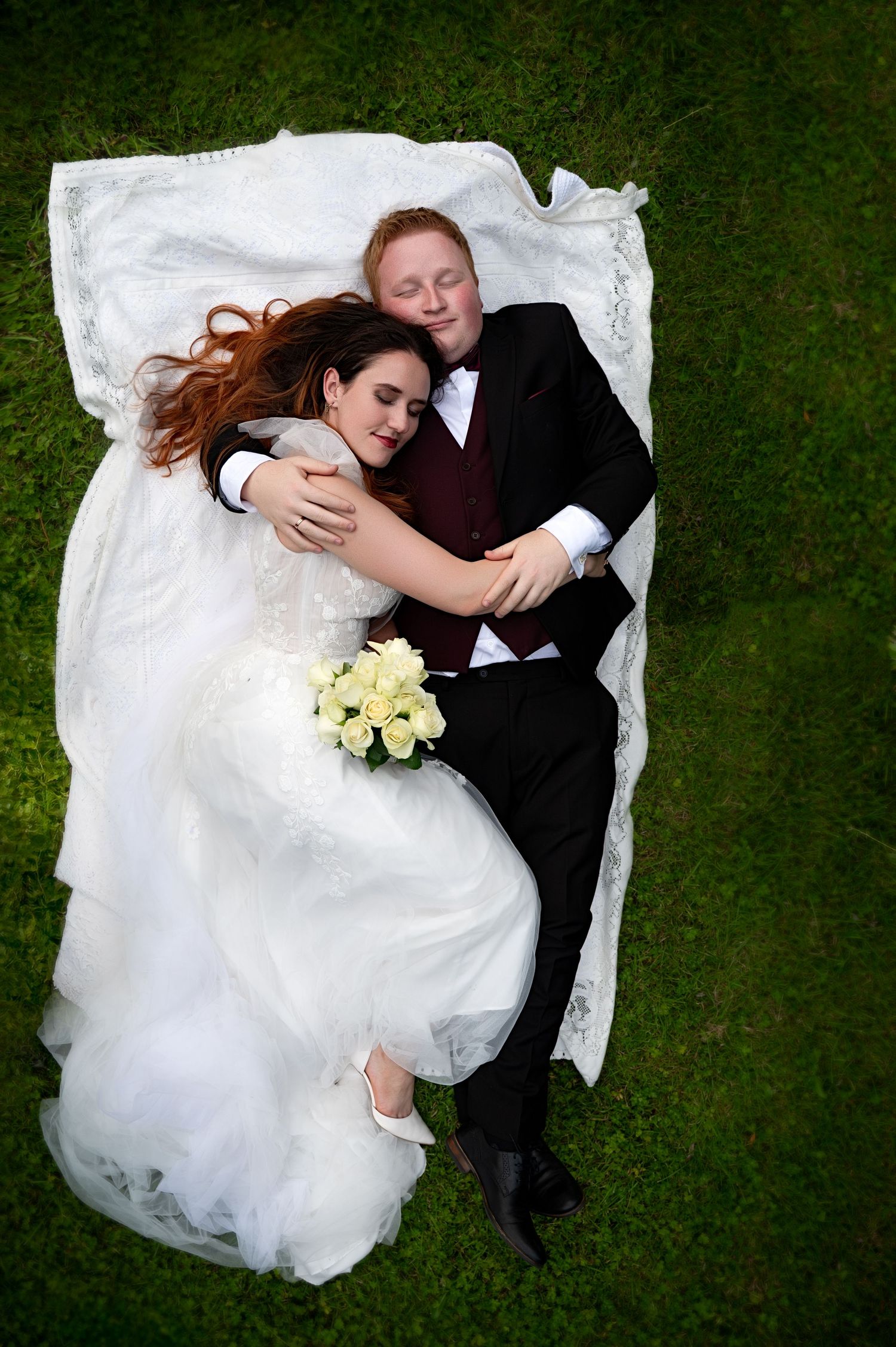Bride lying in the grass with groom cuddled beside her, holding bouquet