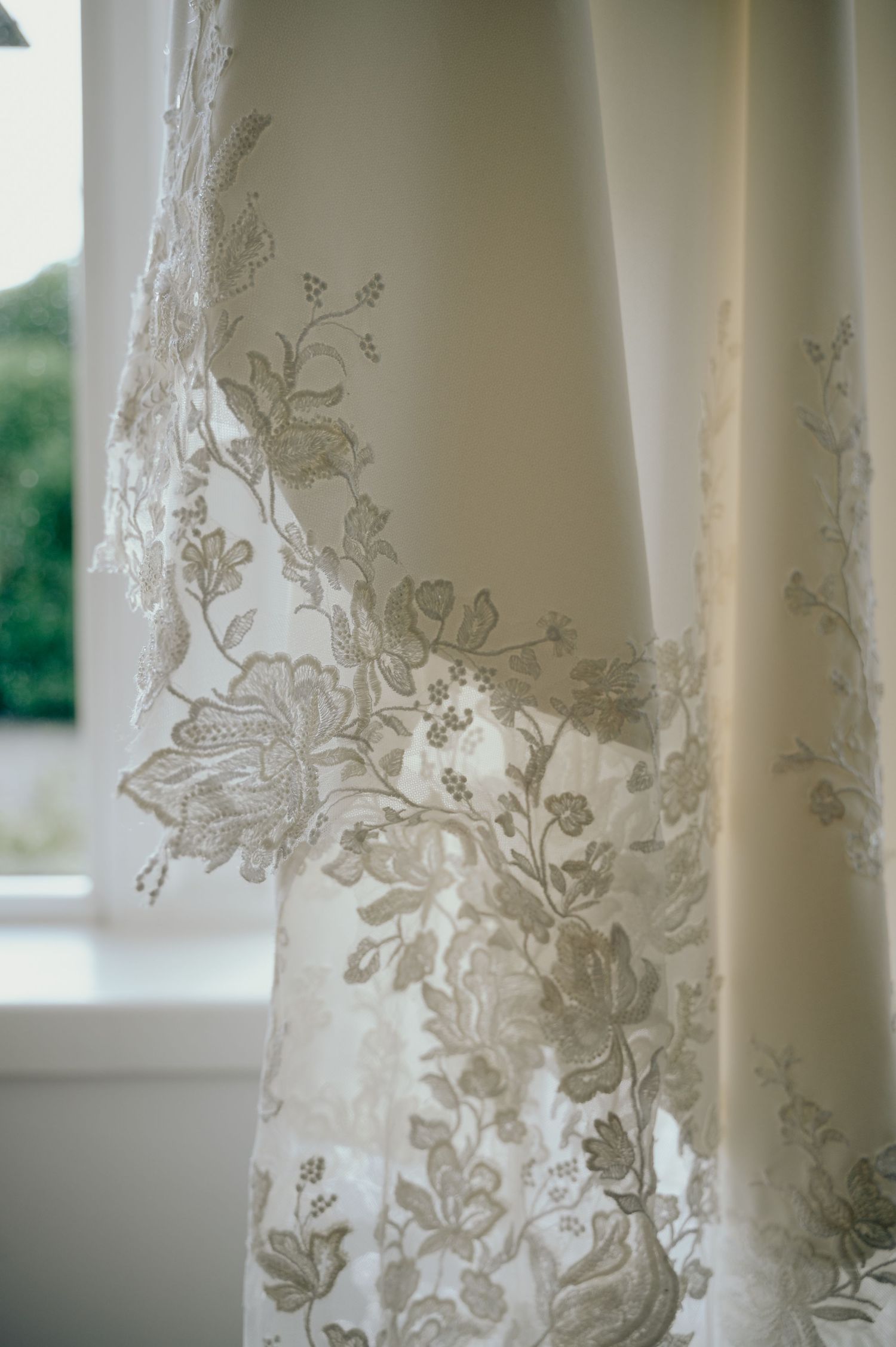 Detail shot of lace hem on the bride’s wedding dress, softly lit by a window