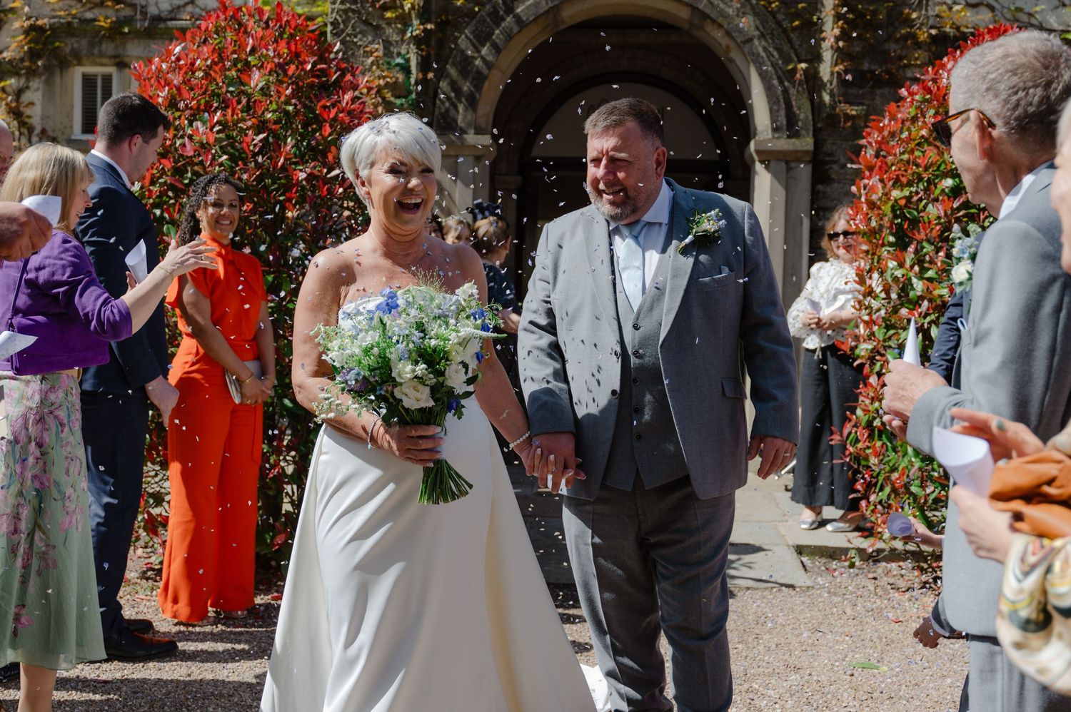 Bride and groom smiling as they exit ceremony surrounded by guests outdoors