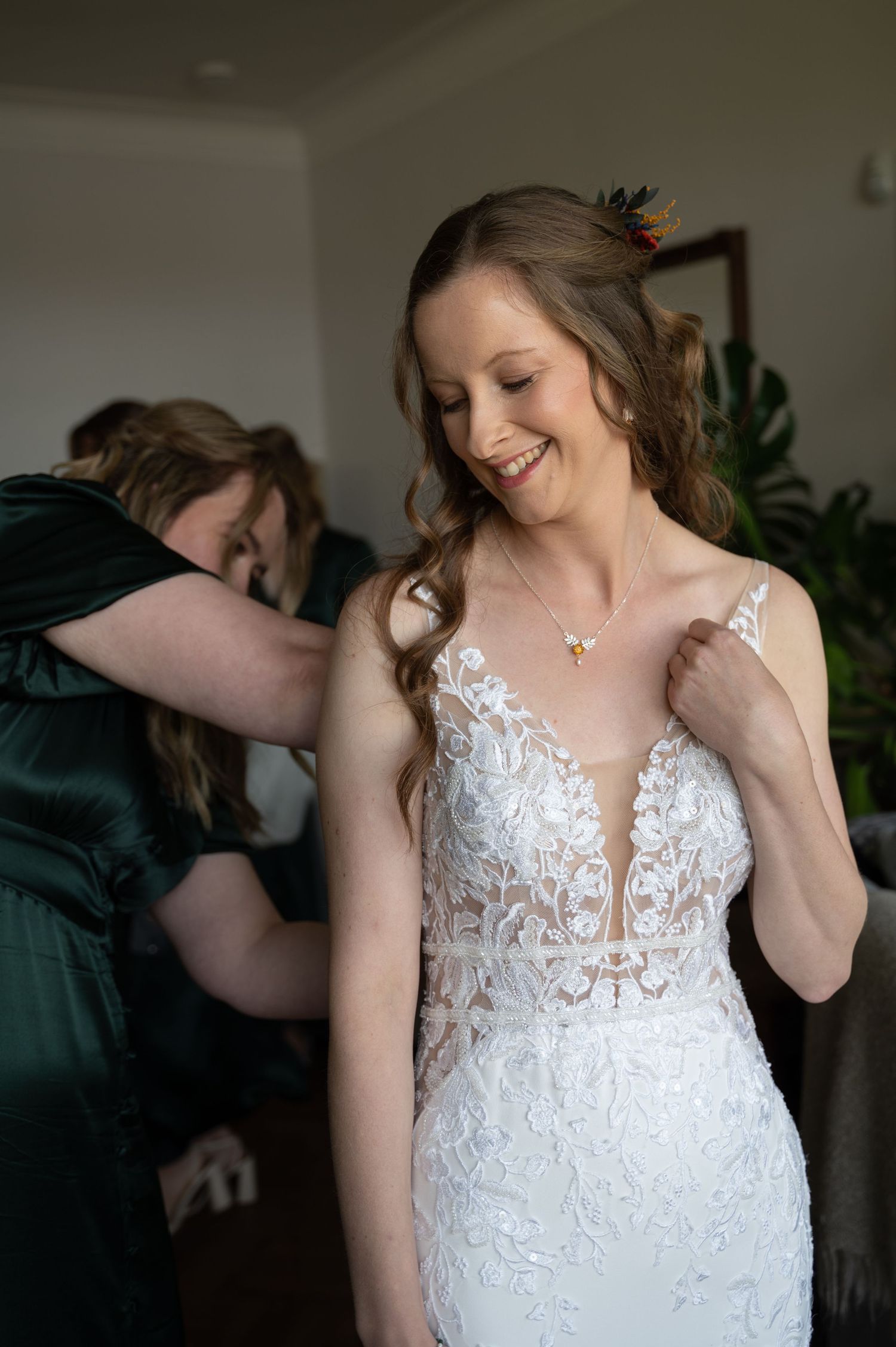 Bridal prep moment as someone helps fasten the back of the bride’s dress