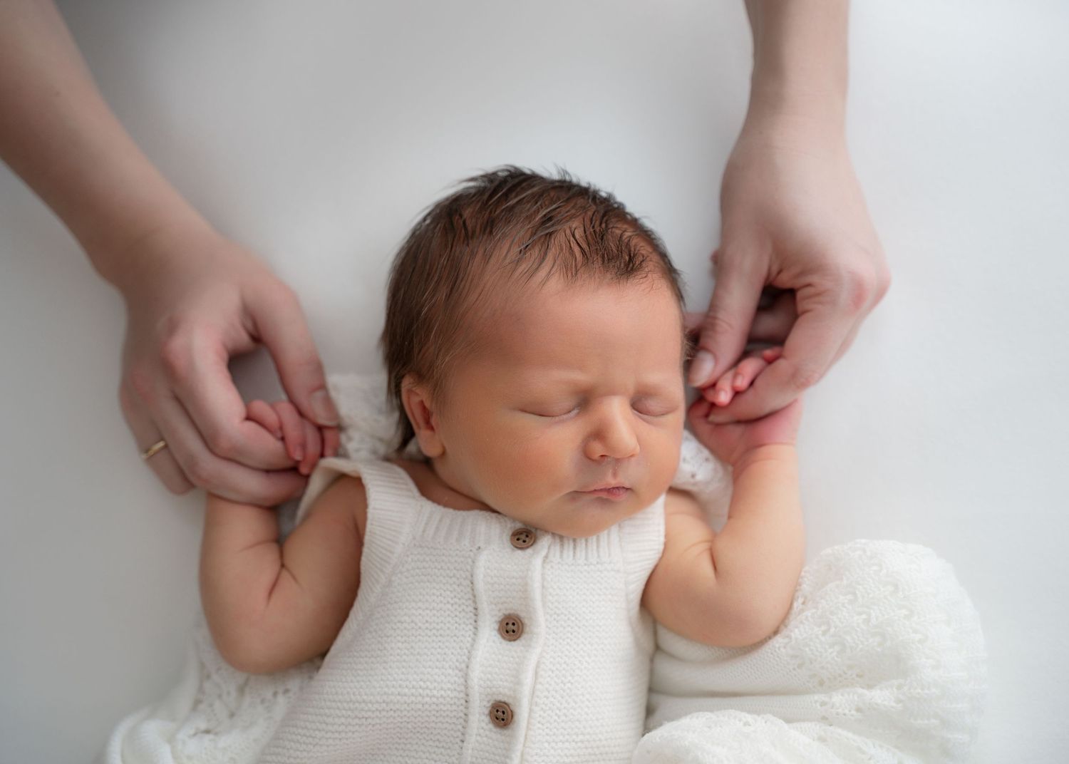 Newborn in a white romper with a parent’s hands gently adjusting the outfit.