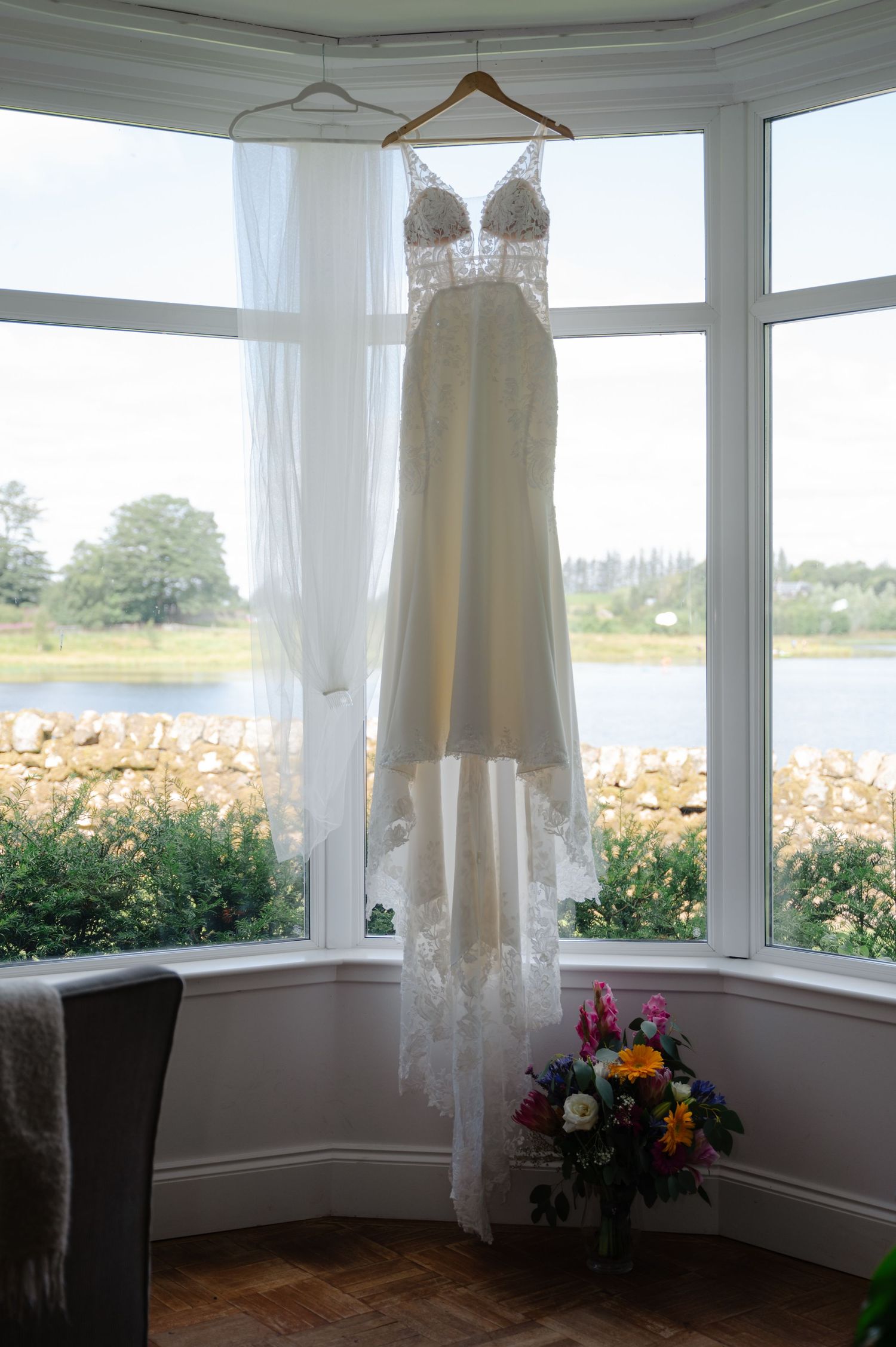 Wedding dress hanging in front of a bay window with countryside views in the background