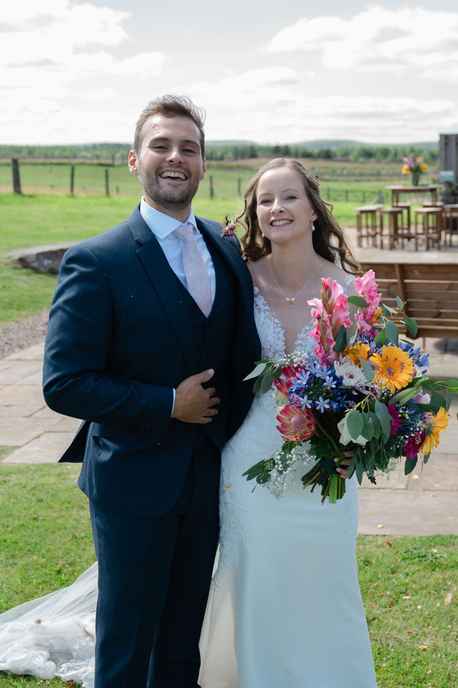 Bride and groom smiling outdoors on wedding day holding colourful bouquet