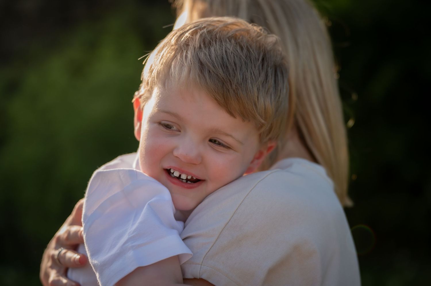 Close-up of a smiling child hugging their parent tightly, radiating warmth and happiness in the golden evening light.