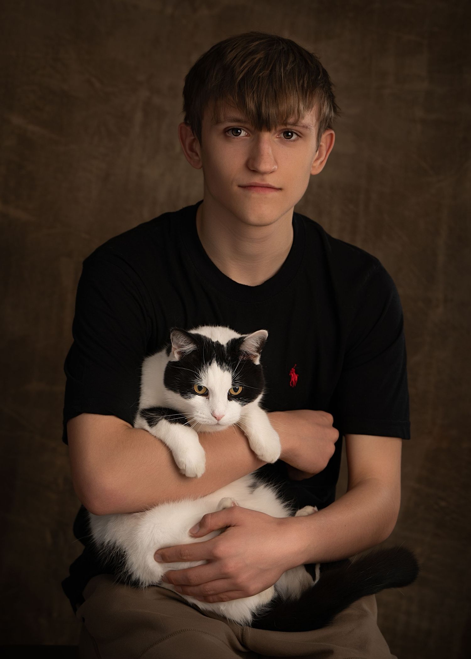 Teen boy seated and holding a newborn baby in his arms.