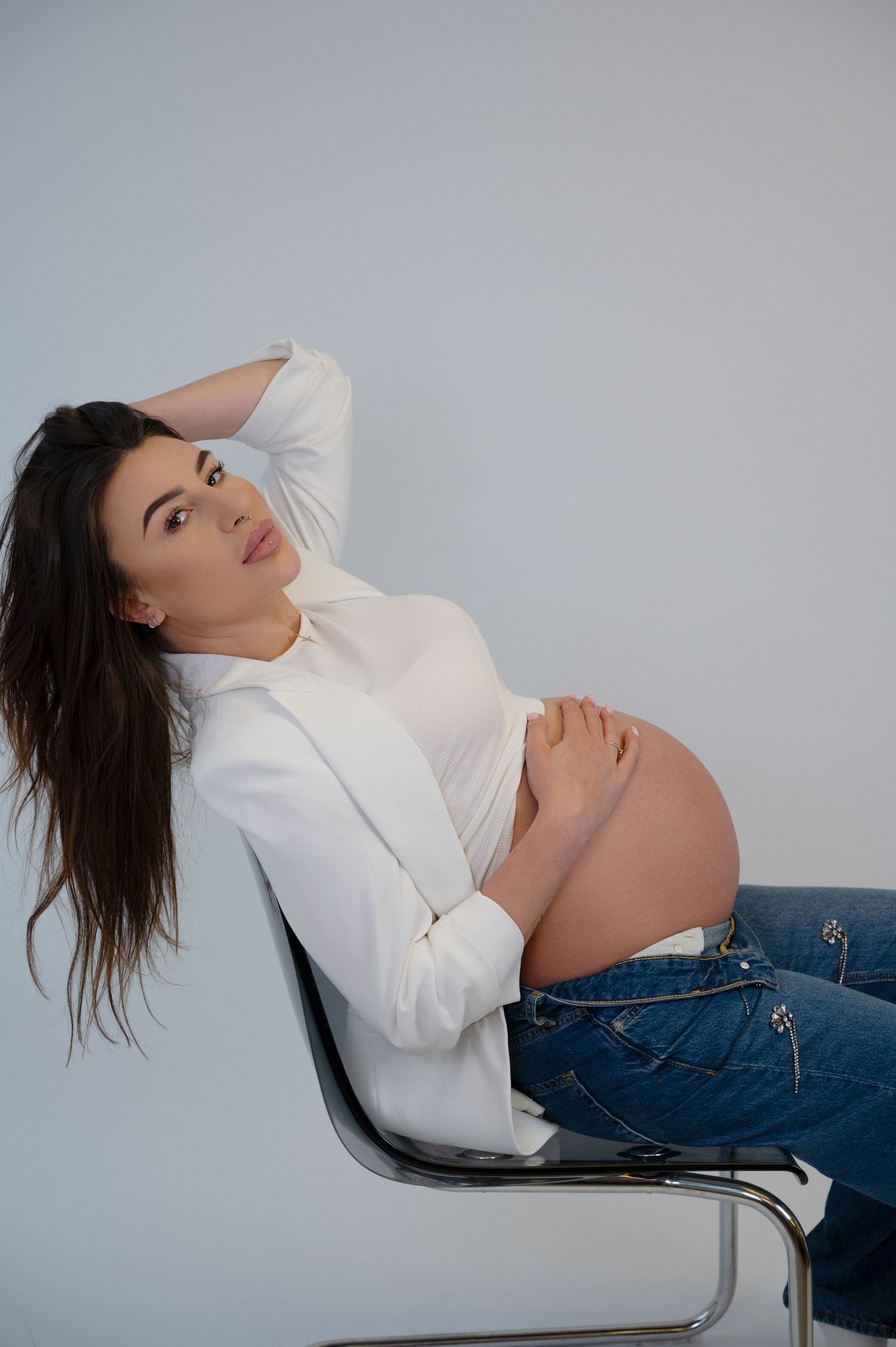 Pregnant woman sitting on a chair in a white top during maternity session