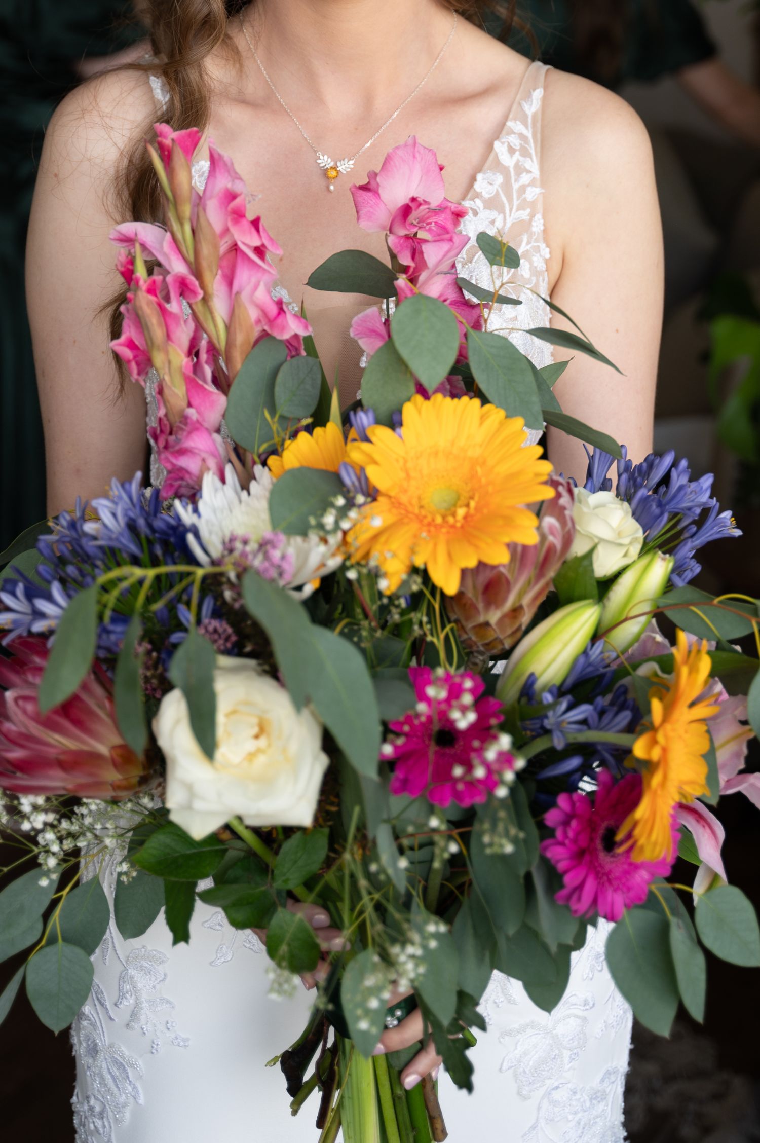 Close-up of bride’s hands holding a colourful wildflower bouquet in her wedding dress