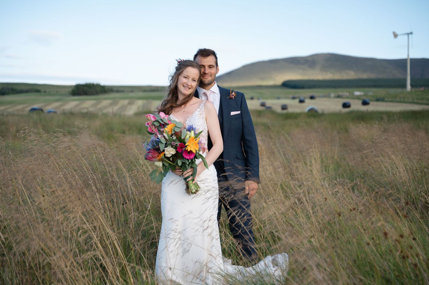 Newlyweds smiling and holding bouquet in wild countryside field