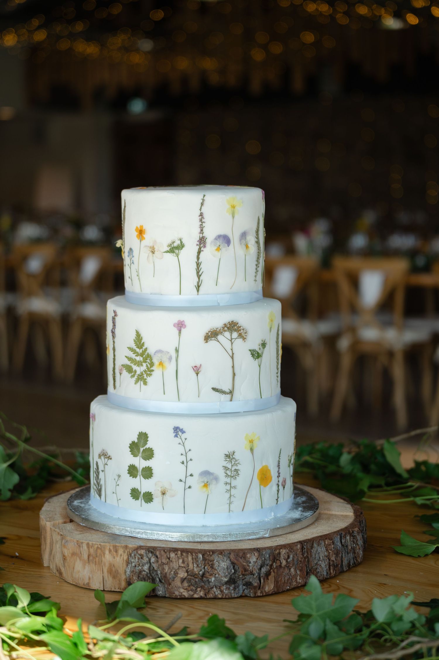 Three-tier rustic wedding cake with floral pressed design, displayed on a wooden barrel