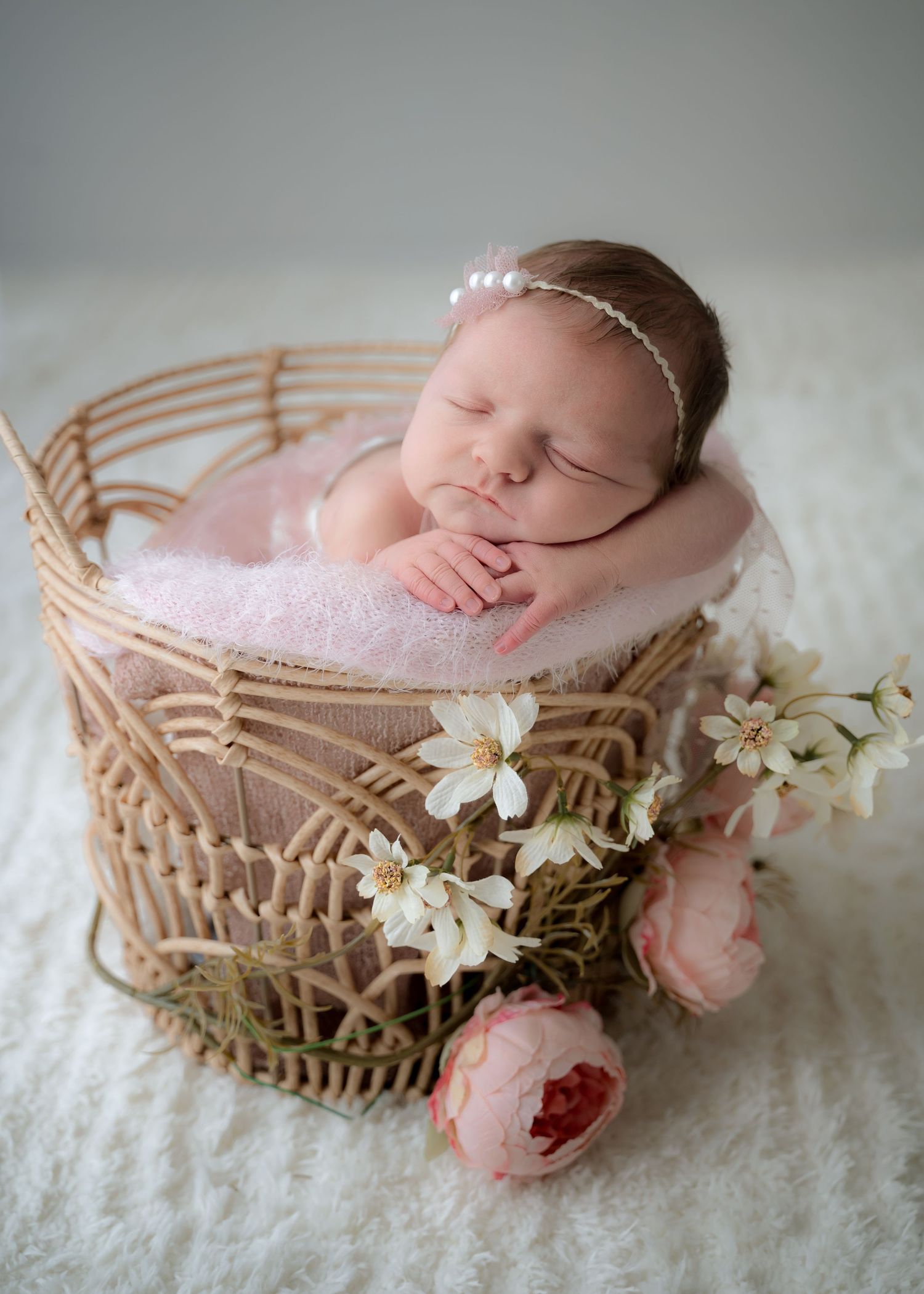 Newborn baby girl sleeping peacefully in a woven basket surrounded by flowers, styled for a natural and cozy newborn photography session.