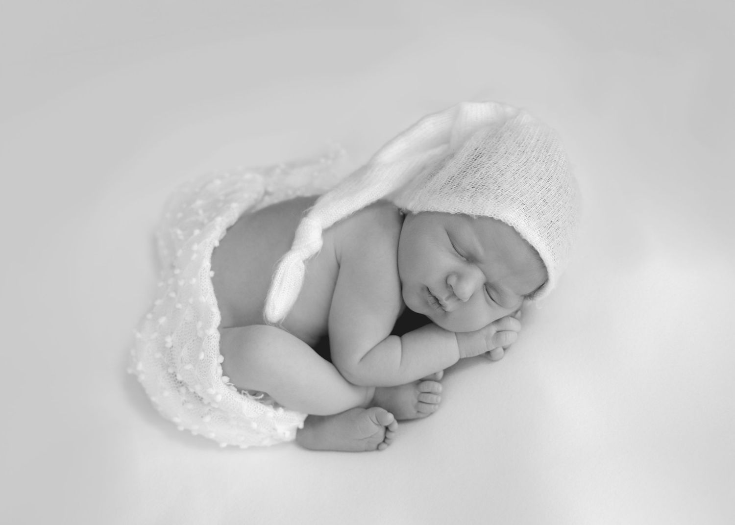 Black and white photo of a newborn wrapped in soft white fabric