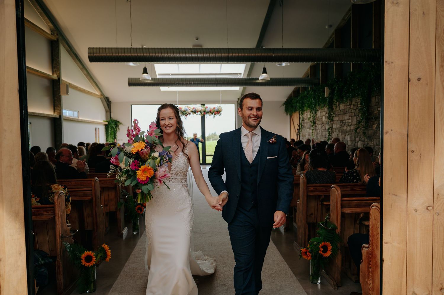 Bride and groom entering indoor ceremony space hand in hand, smiling