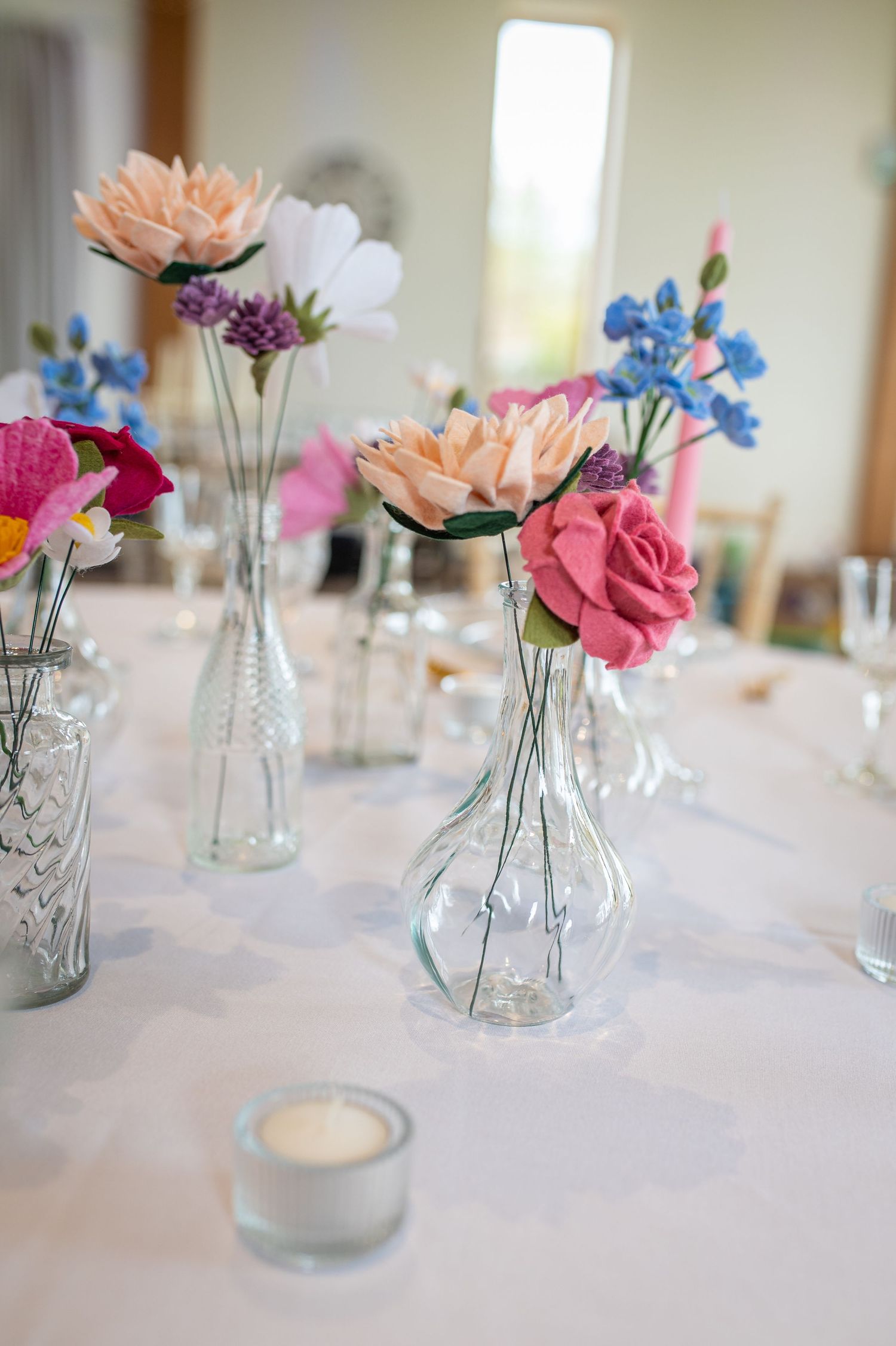 Elegant wedding reception table setup with crystal glasses, pastel flower arrangements, and soft candlelight in a bright, airy venue.