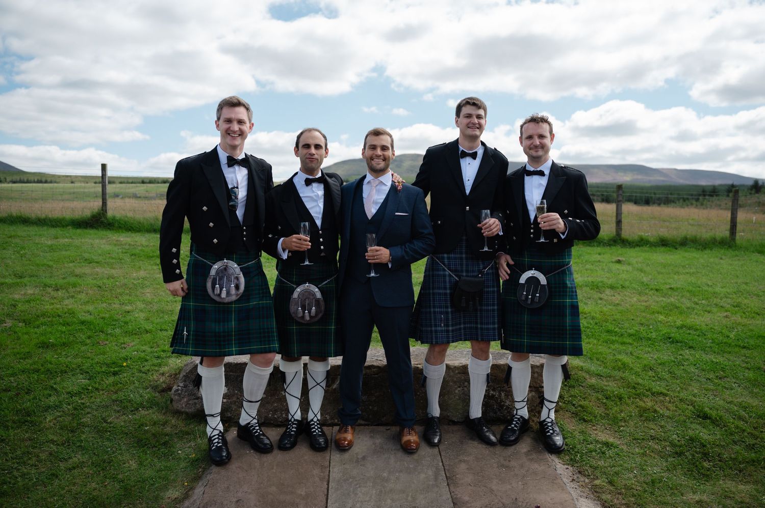 Group of groomsmen wearing traditional kilts, standing outdoors before the ceremony
