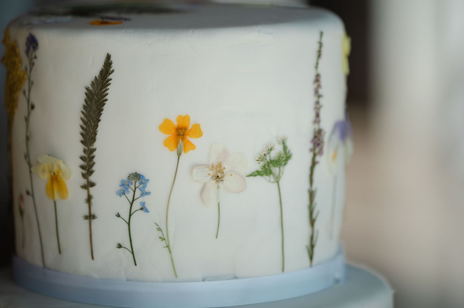 Single-tier white wedding cake decorated with pressed wildflowers