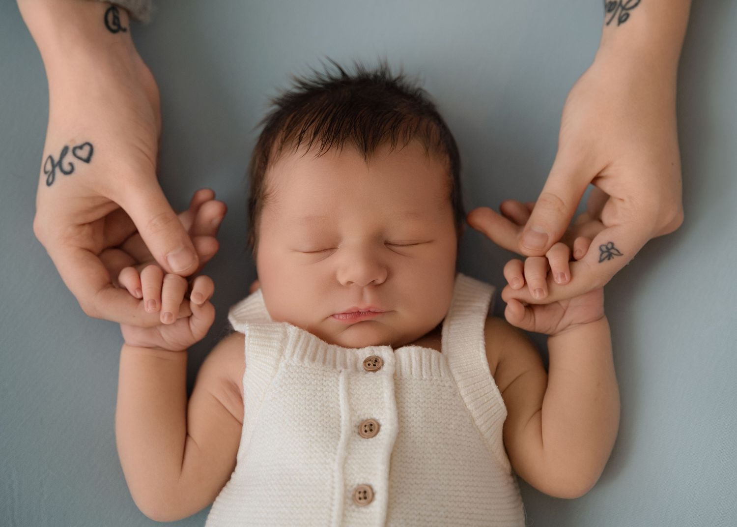 Sleeping baby holds onto parents' fingers on a soft blue blanket.
