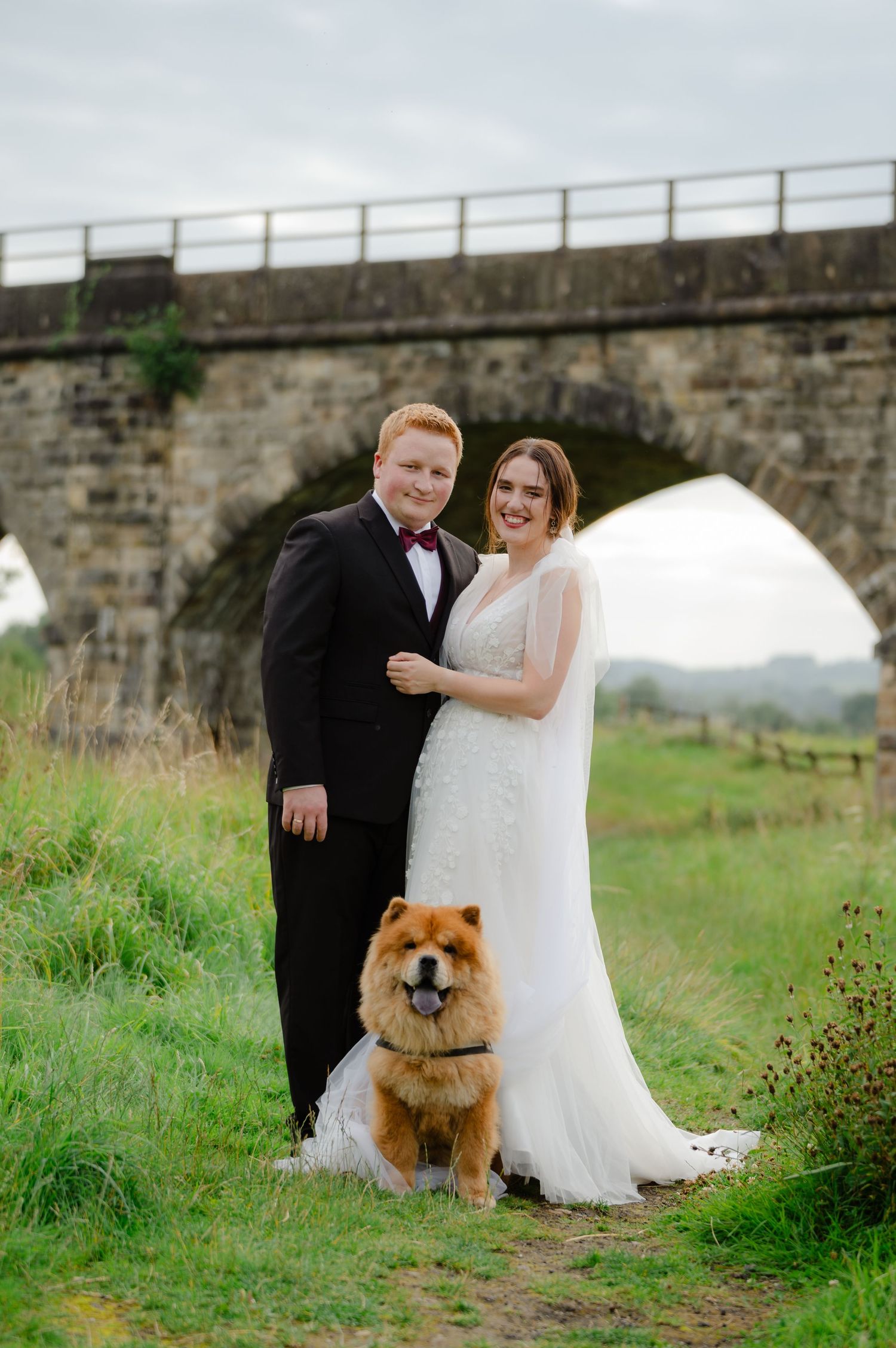Couple standing in front of a stone viaduct with their dog at their feet
